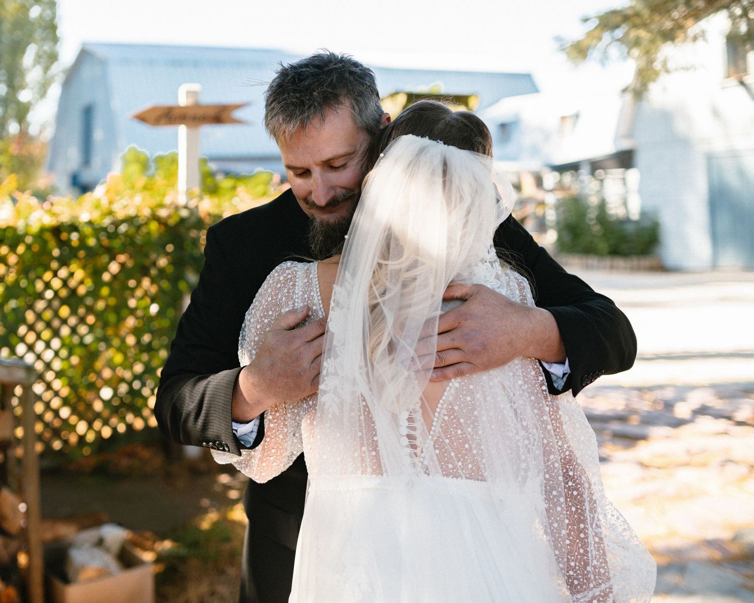 Emotional father-daughter first look embrace at outdoor wedding venue in warm sunlight.