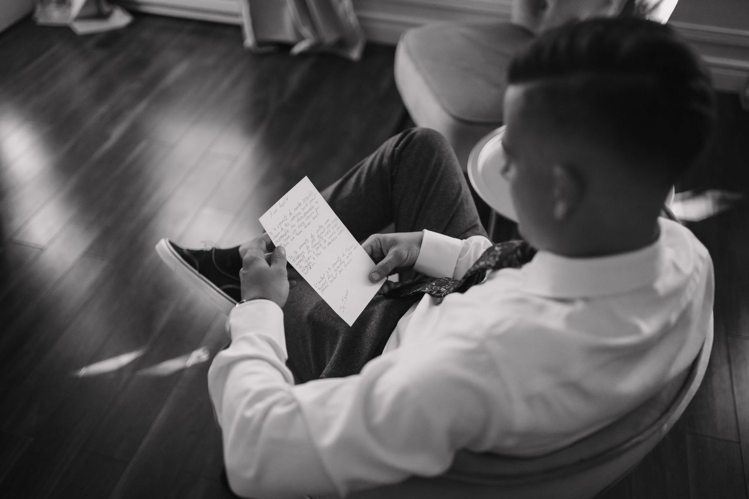 Groom reading a heartfelt letter while seated on the floor in black and white wedding photo.