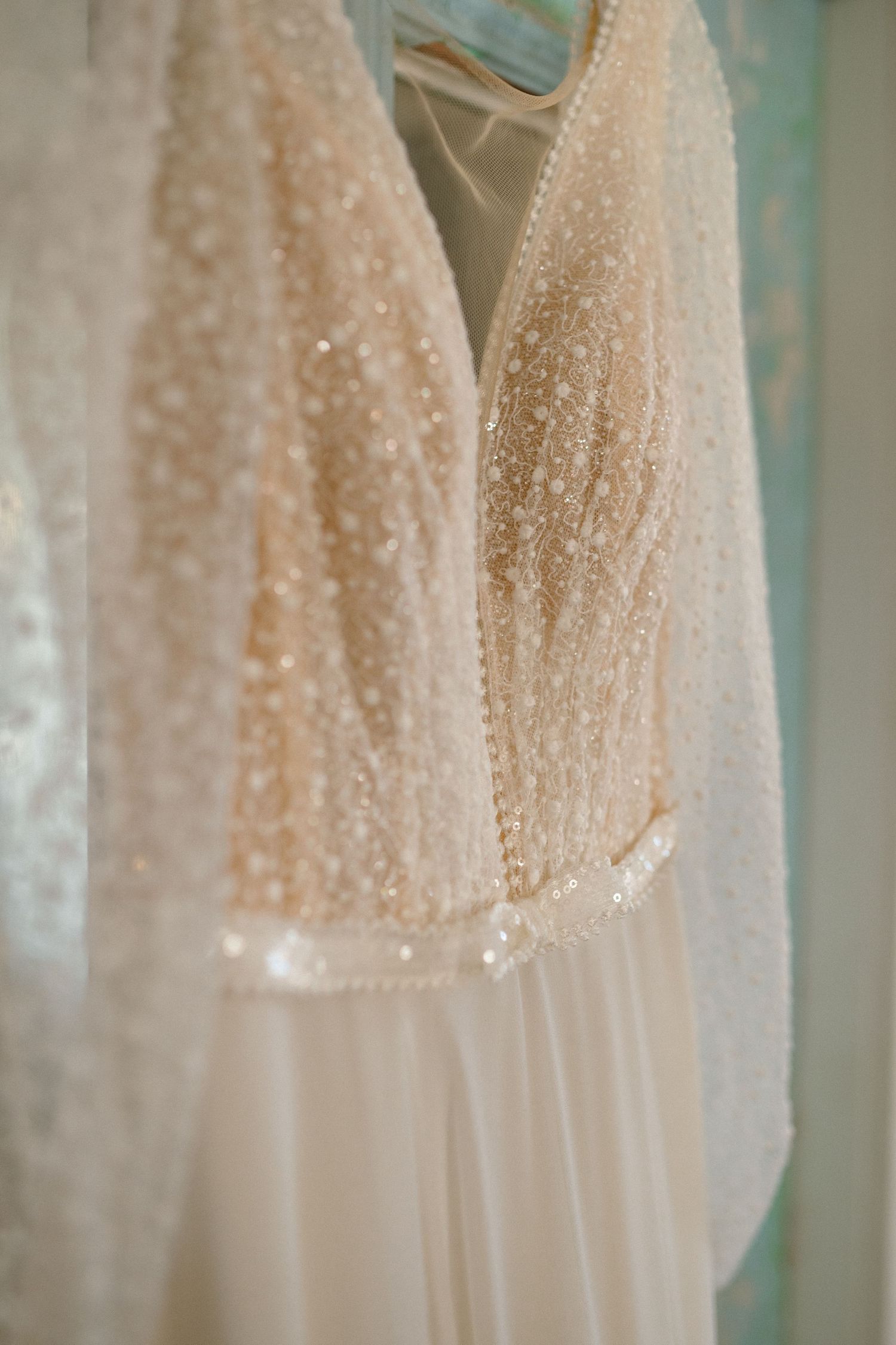 Close-up of a beaded champagne wedding gown with pearl embellishments hanging on a hanger.