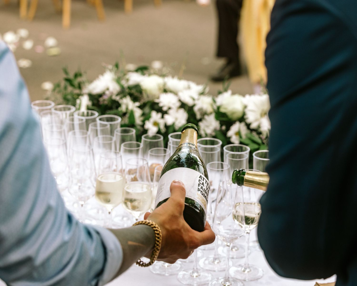 Person pouring champagne into elegant glasses at a wedding reception with white floral arrangements.