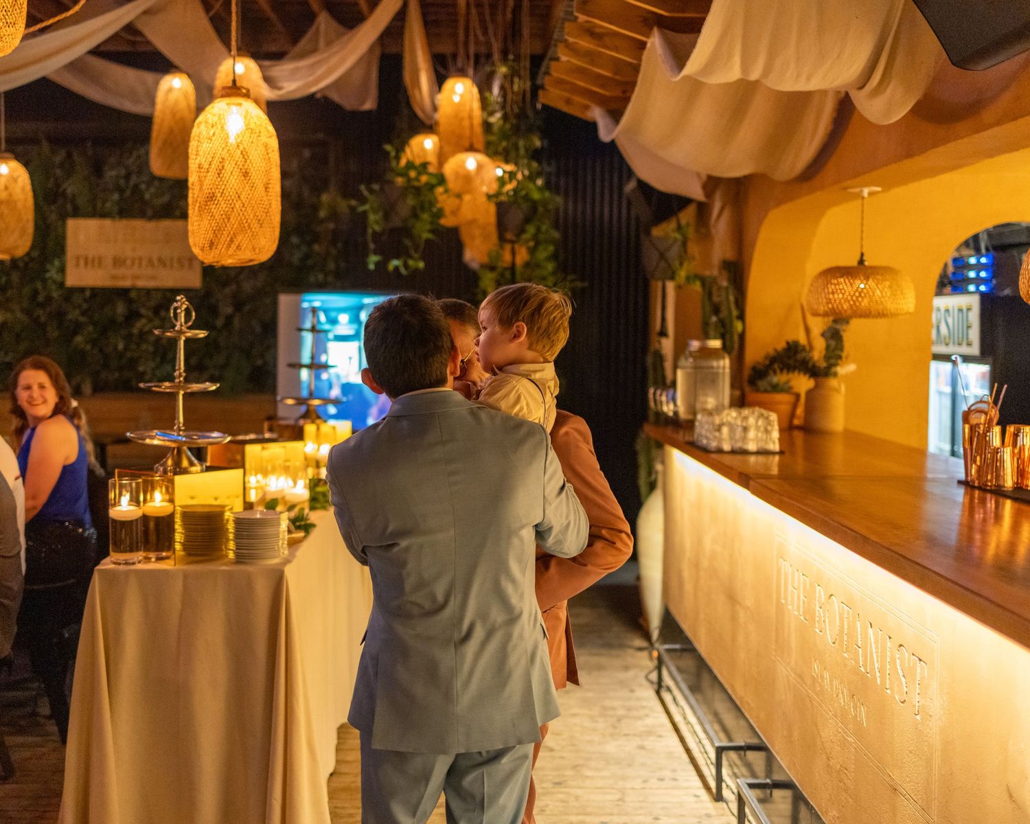 Couple sharing a romantic kiss at an elegant wedding reception bar with warm hanging lanterns.