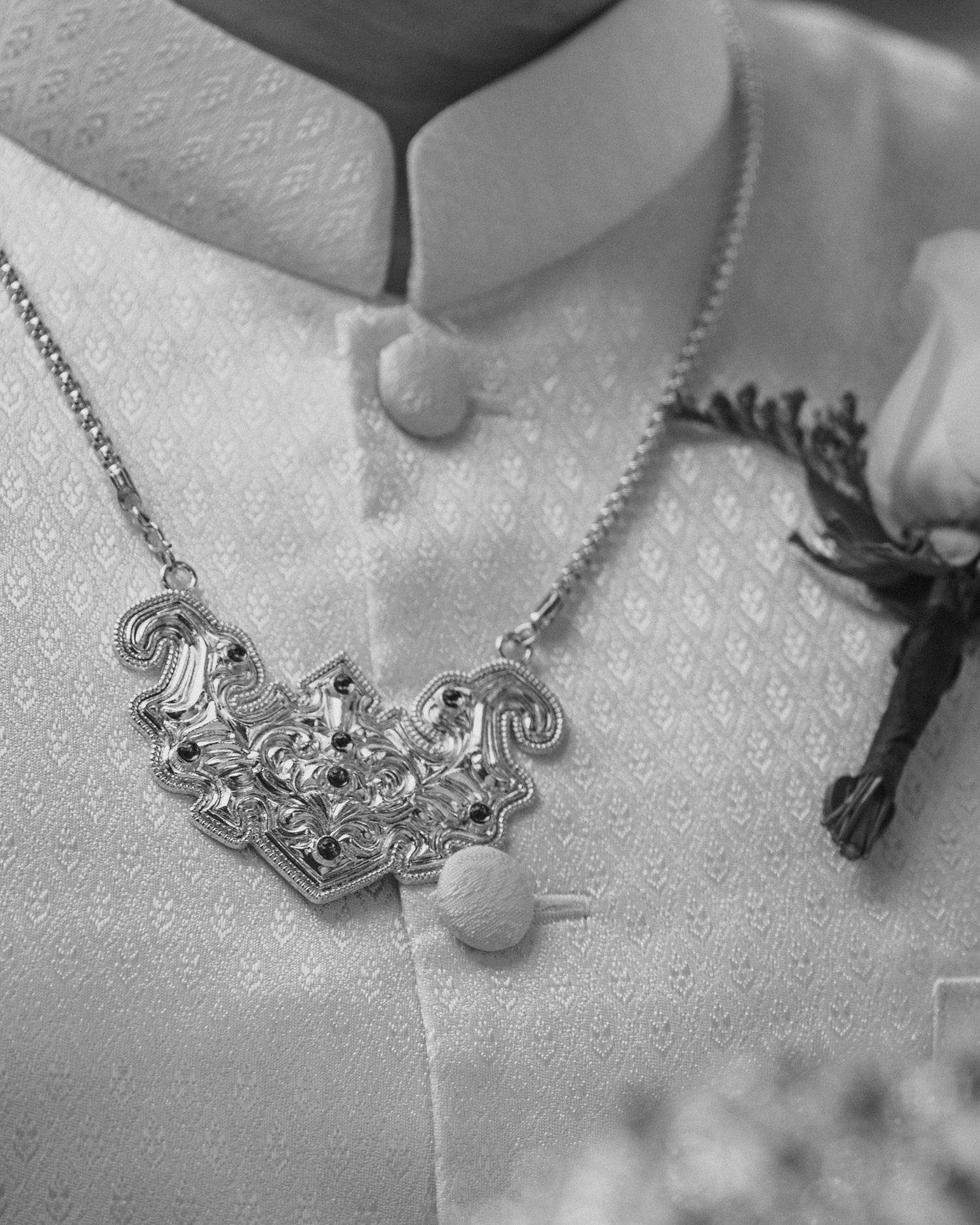 Close-up of an ornate silver bridal necklace on a groom wearing a white embroidered wedding suit.