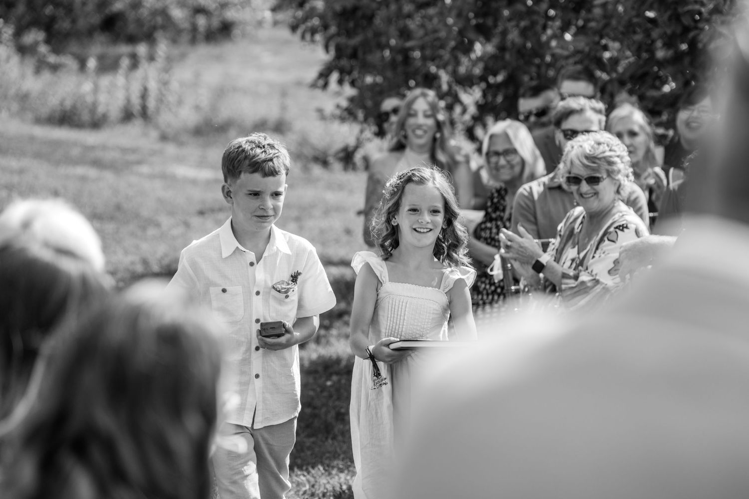 Children walk in outdoor wedding ceremony procession in black and white photo.