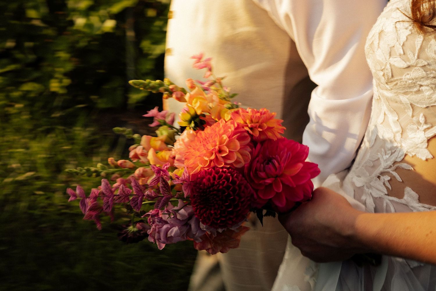 Close-up of colorful bridal bouquet with dahlias held by couple.