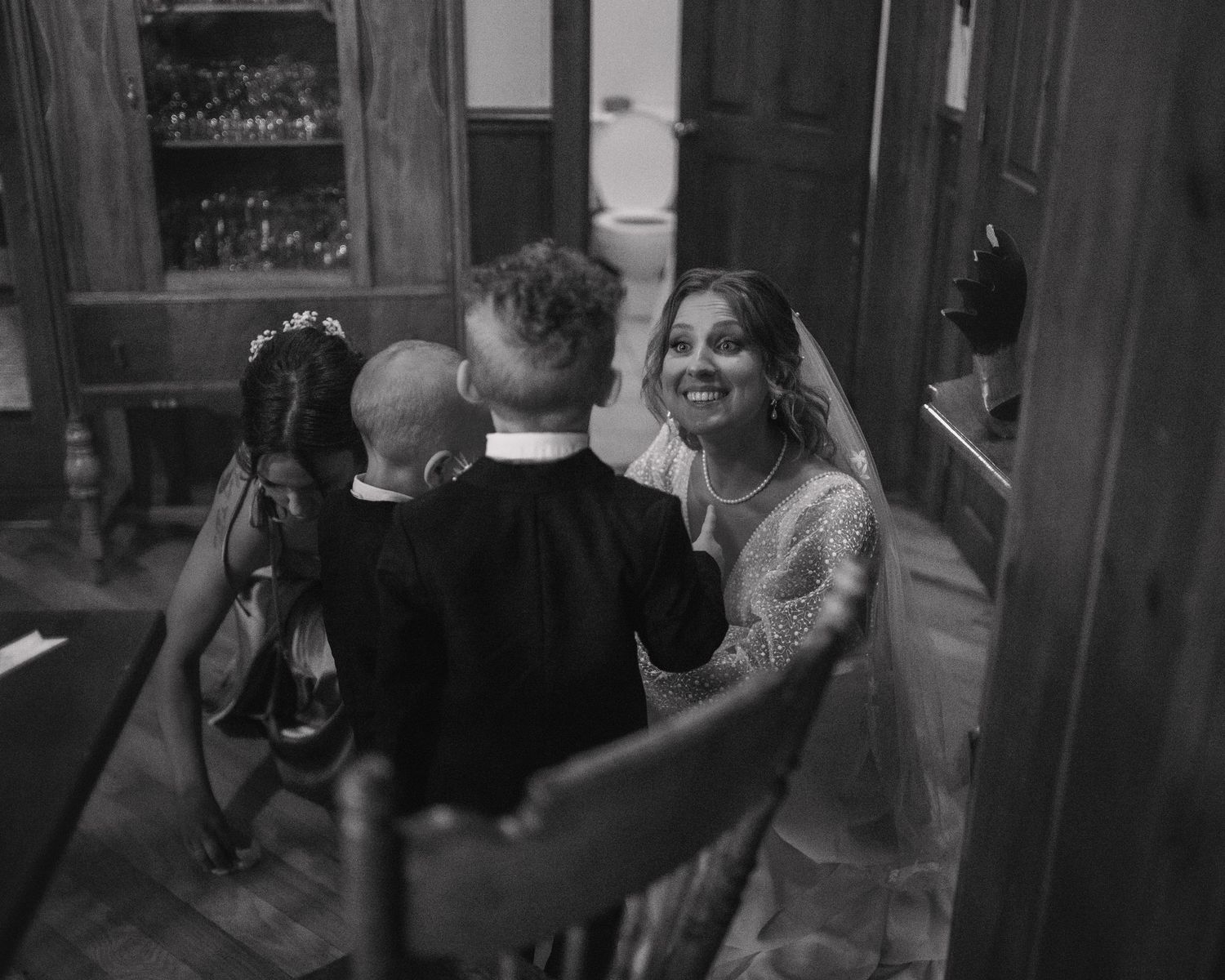 Bride smiling joyfully at groom during intimate wedding ceremony in rustic interior, black and white.
