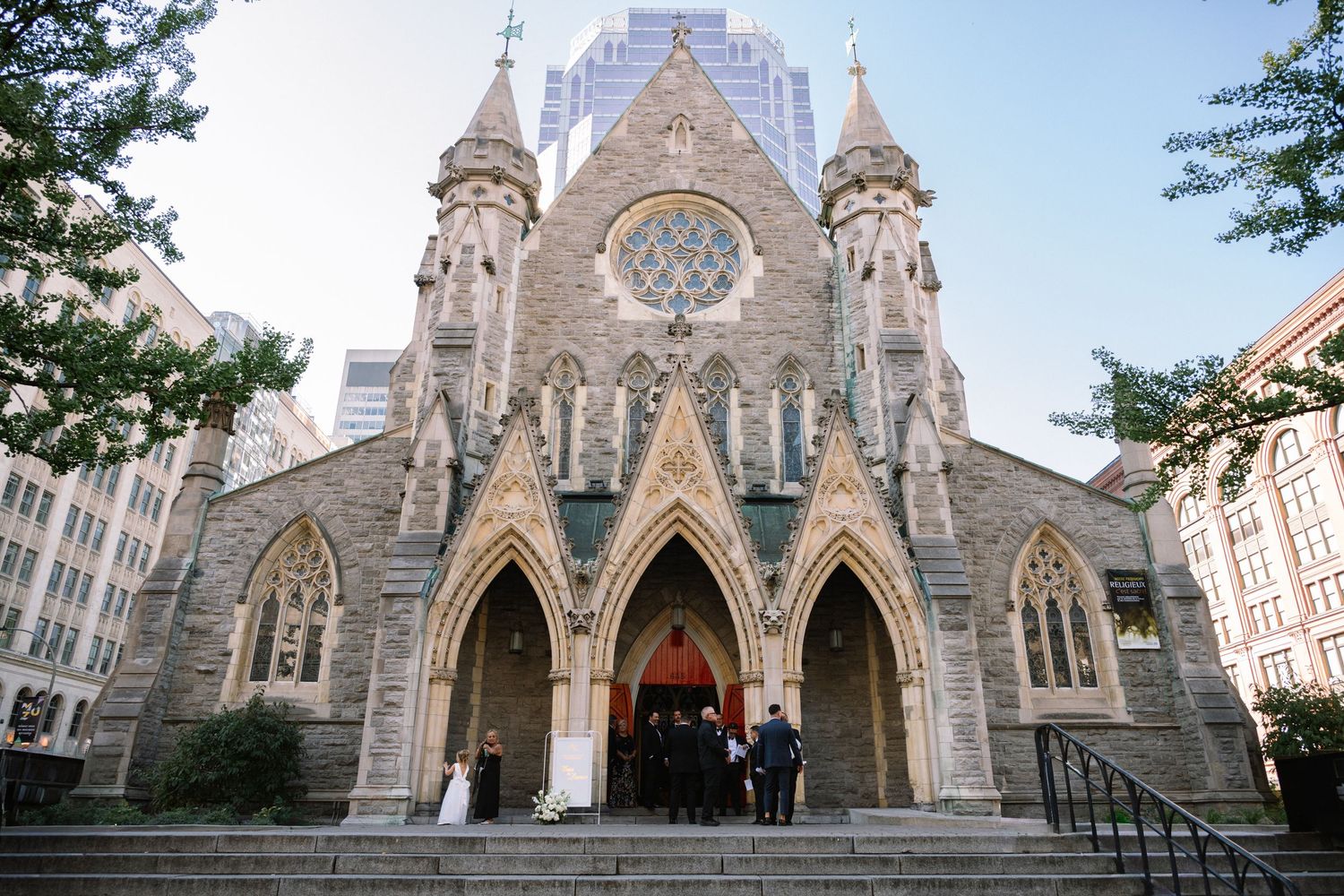 Wedding couple poses on steps of grand Gothic stone church with arched doorways and rose window.