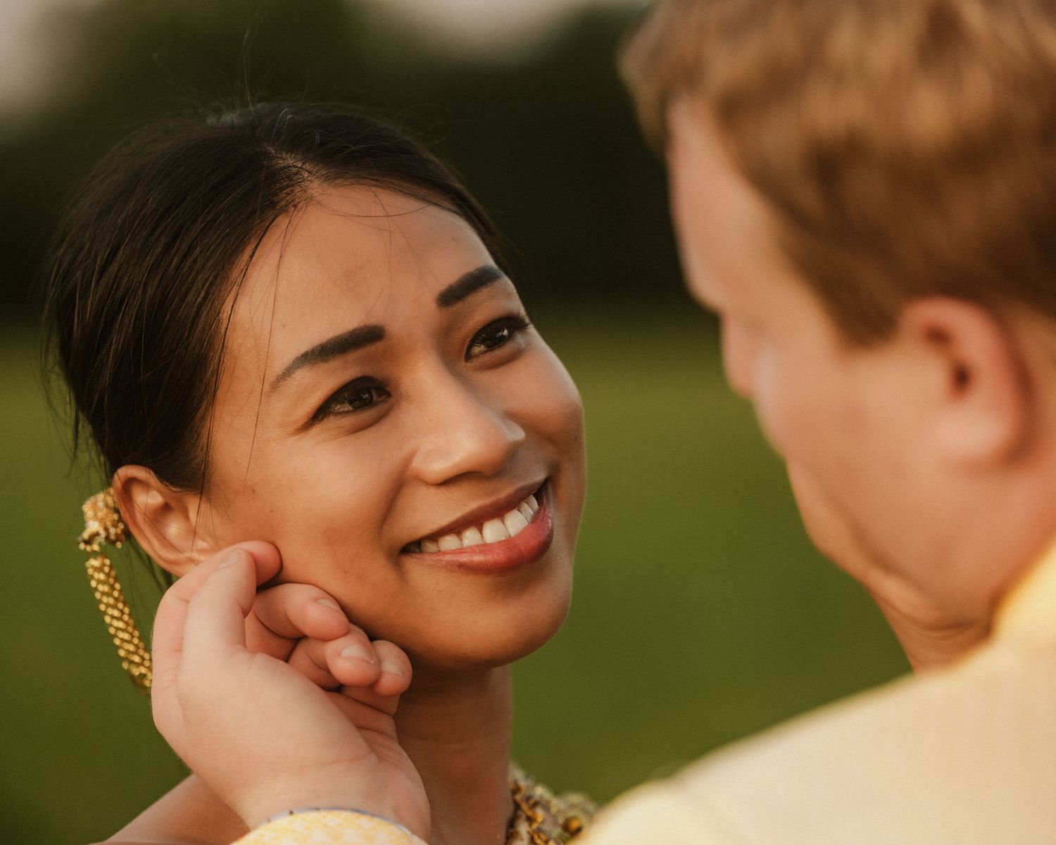 Smiling woman with gold earrings gazes at her partner during a romantic outdoor engagement session.