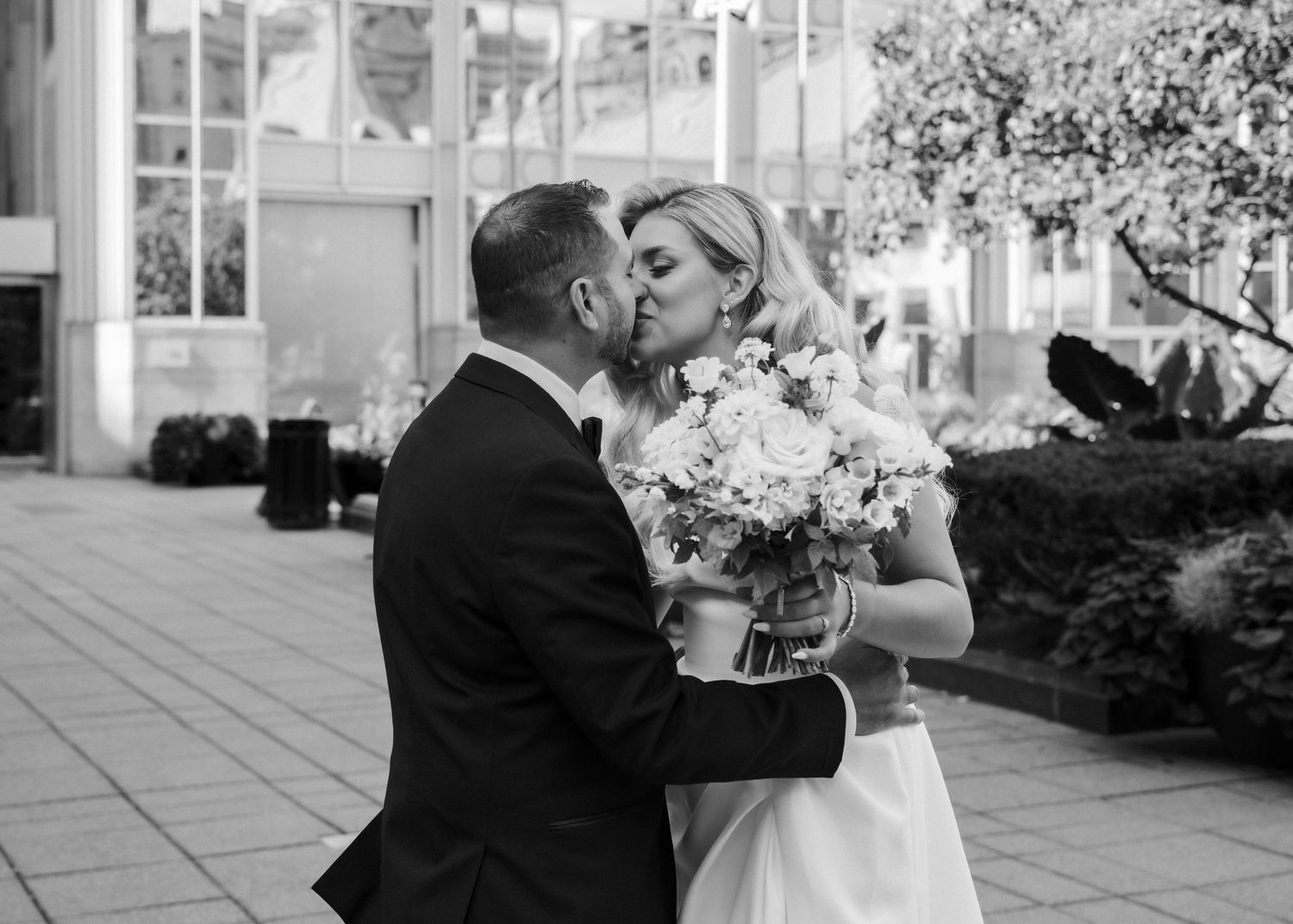 Black and white wedding photo of a bride and groom sharing a kiss while holding a bouquet.
