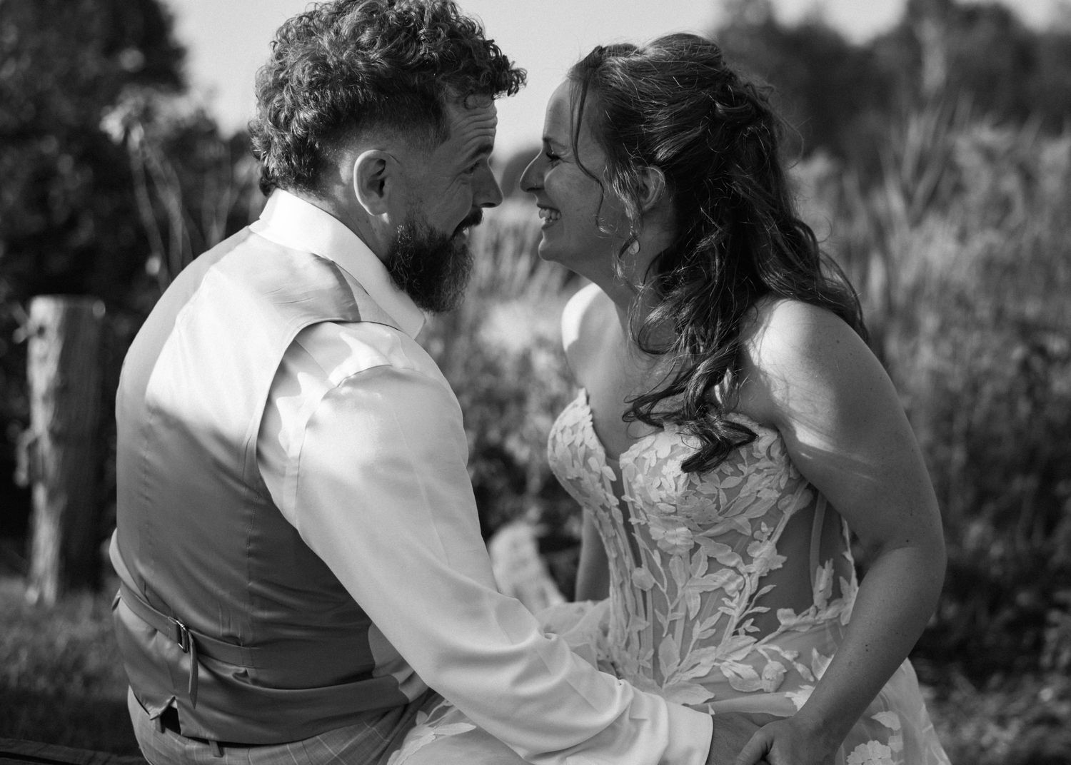 A bride and groom share an intimate moment, nearly kissing, in a black and white outdoor wedding portrait.