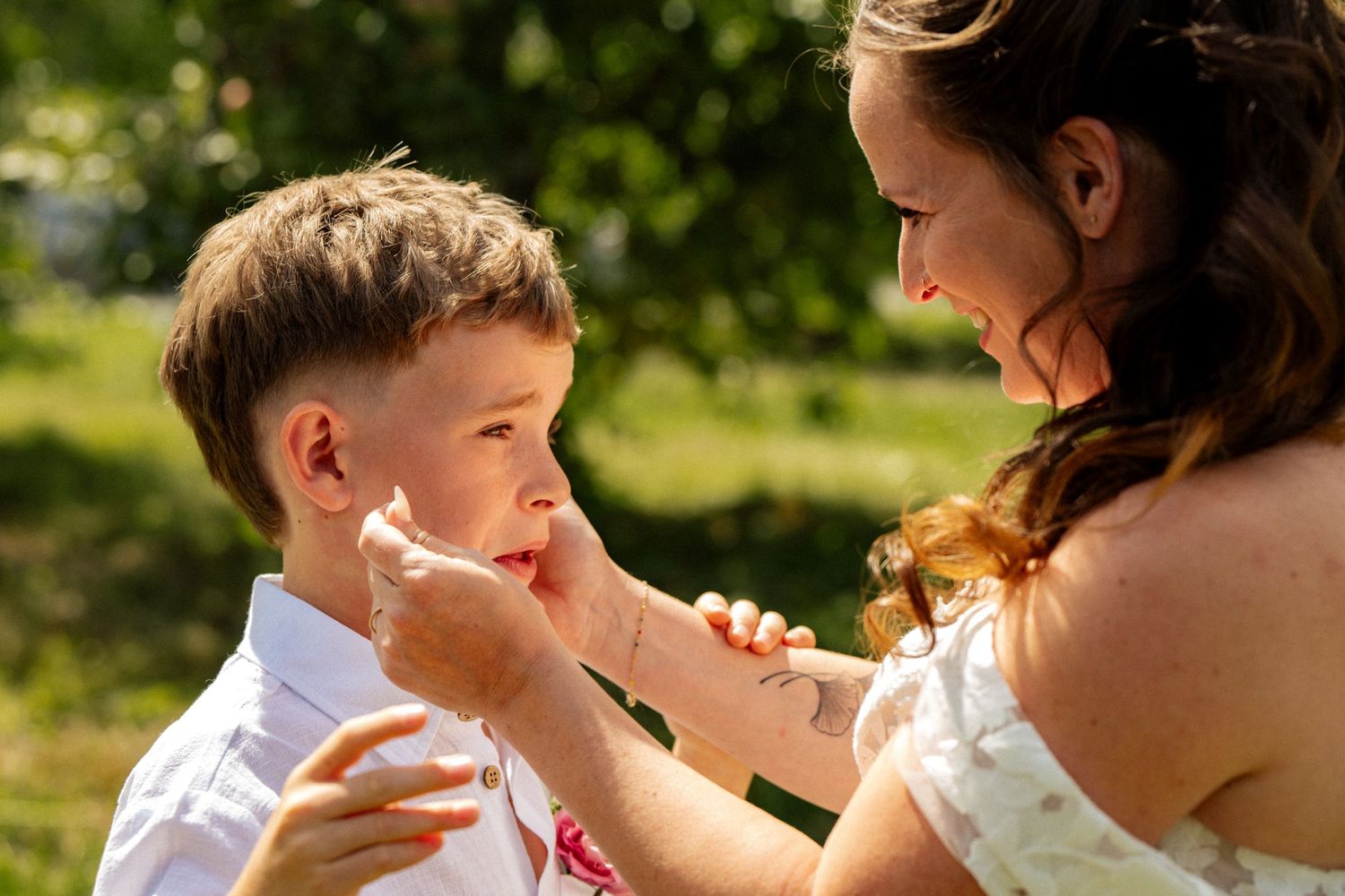 Mother tenderly wiping young son's face outdoors at a sunny wedding celebration.