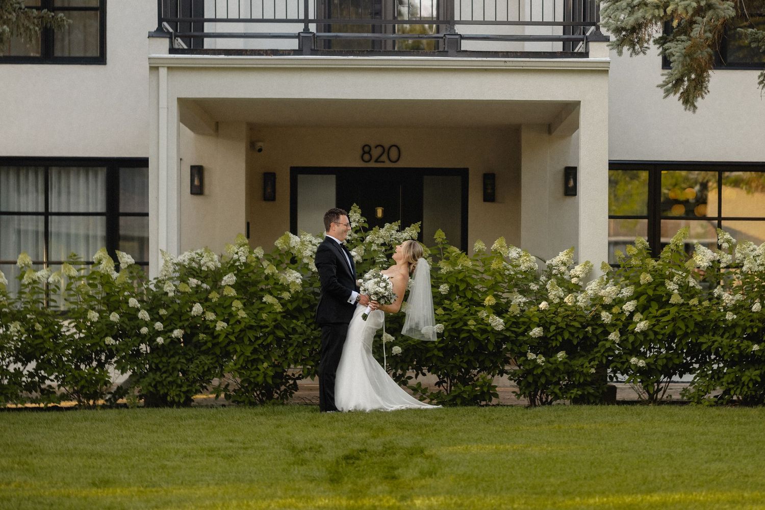 Bride and groom share romantic moment outside elegant white building 820 surrounded by lush white florals.