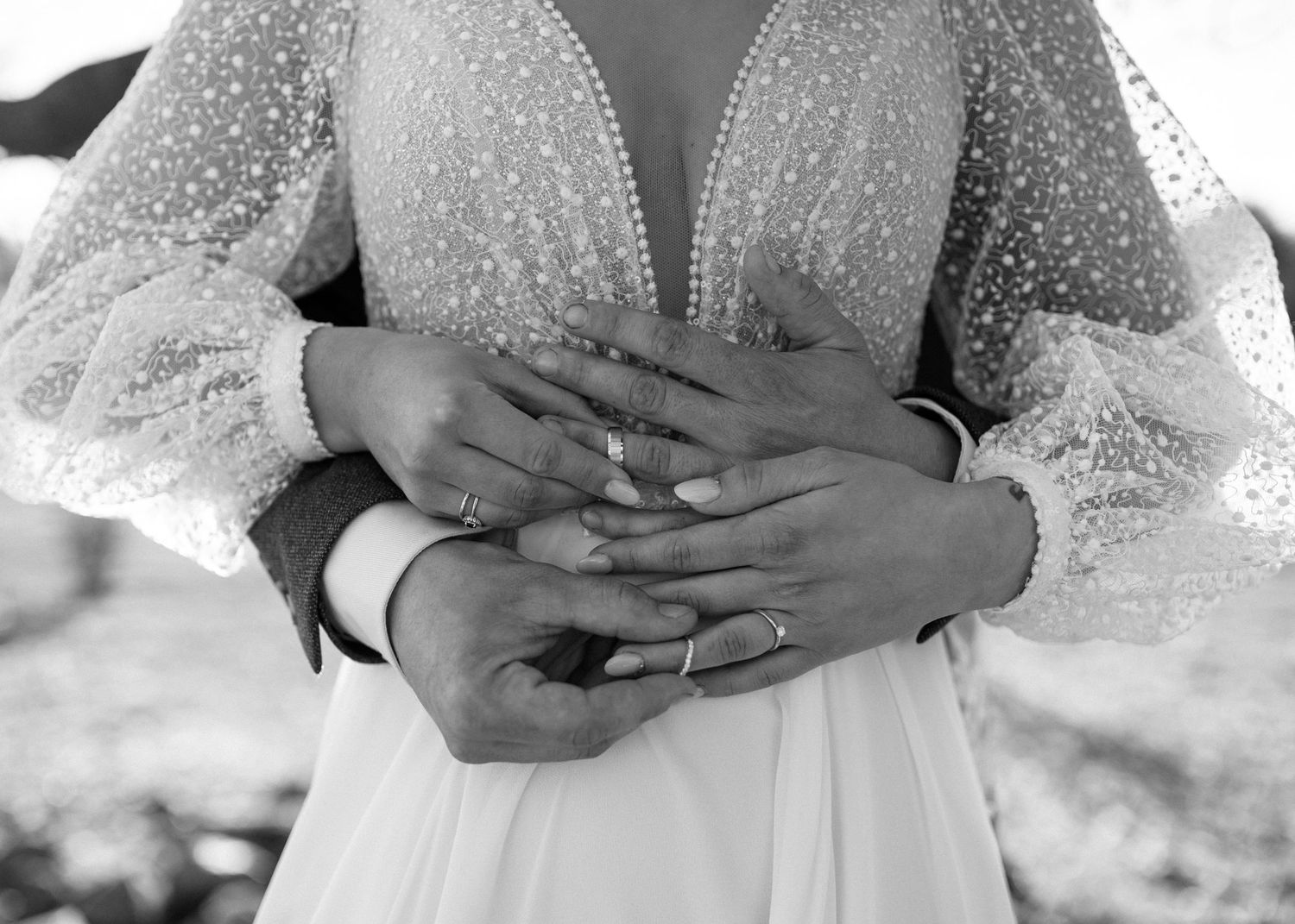 Black and white close-up of couple embracing, showing wedding rings on bride in pearl-dotted gown.