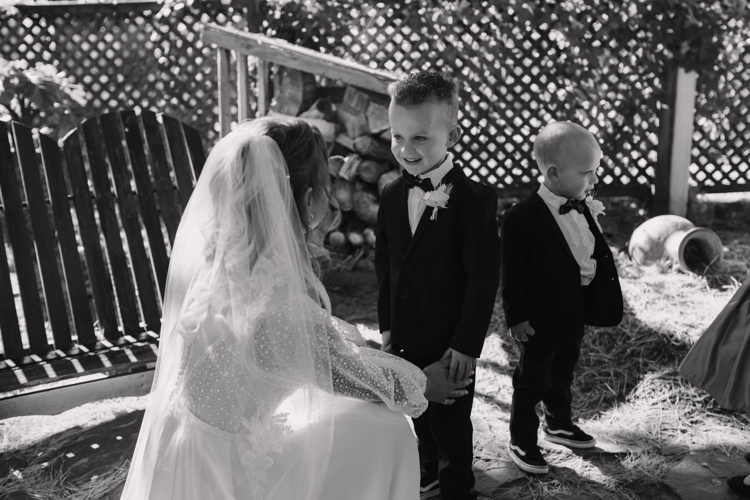 Black and white photo of bride in lace veil kneeling with two young boys in tuxedos.