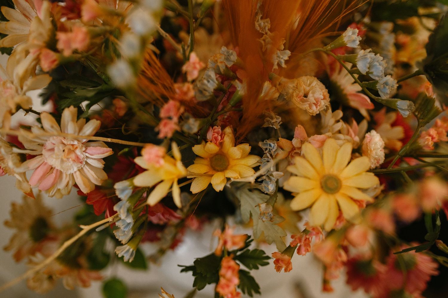 Close-up of a vibrant autumn wedding bouquet with yellow daisies, pink and orange dried flowers.
