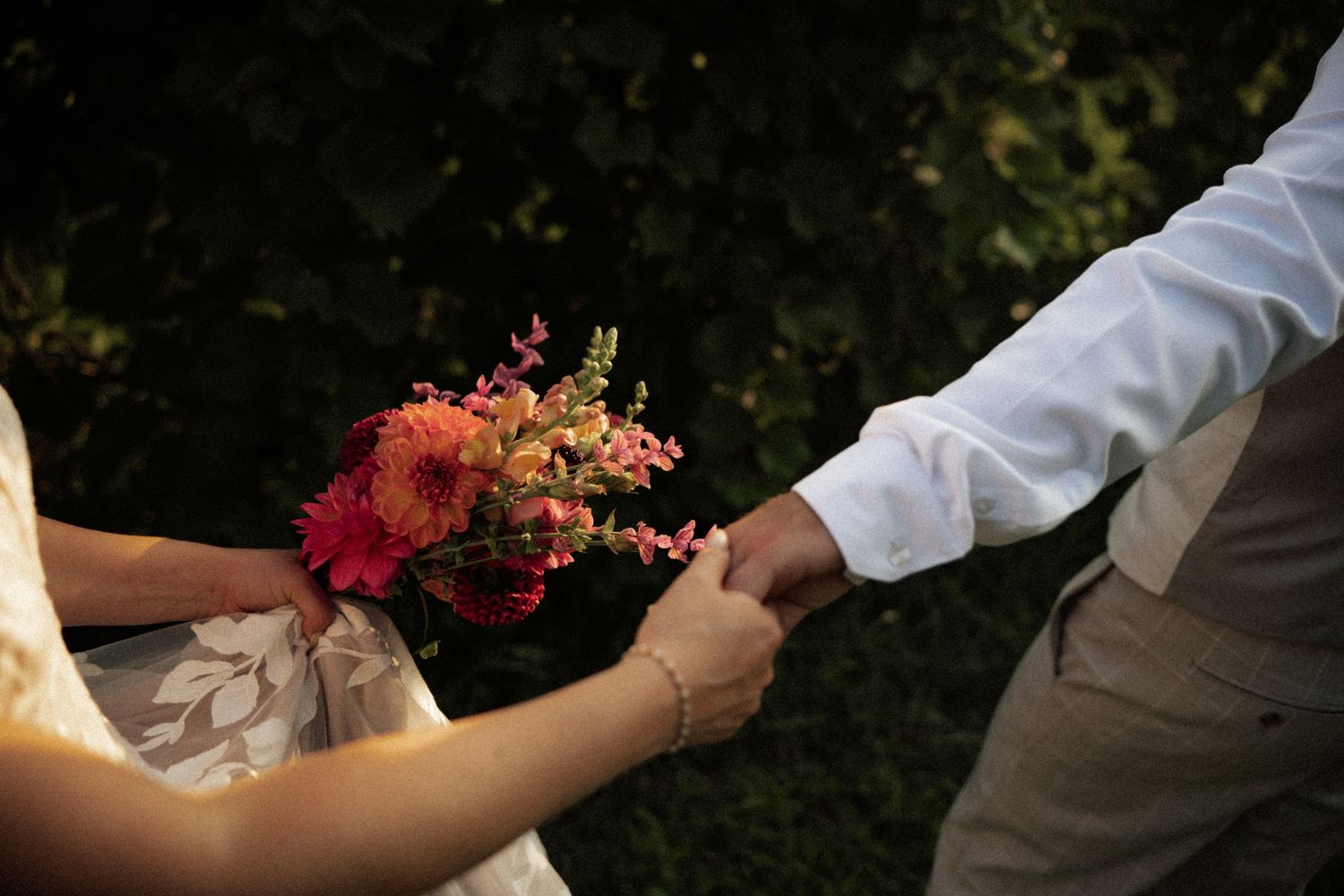 Bride and groom holding hands exchanging colorful wedding bouquet of pink and orange flowers.