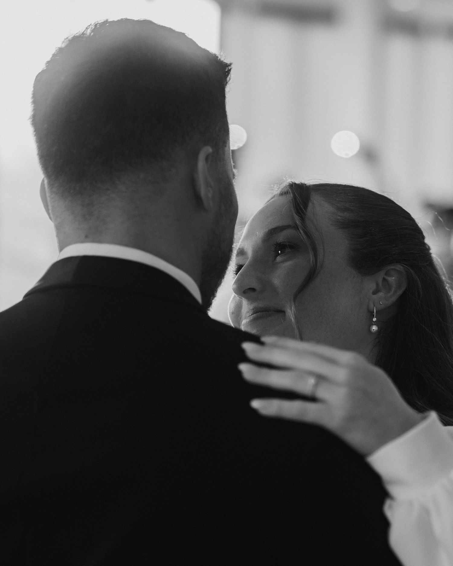 Black and white wedding photo of a couple sharing an emotional first dance, bride gazing up at groom.