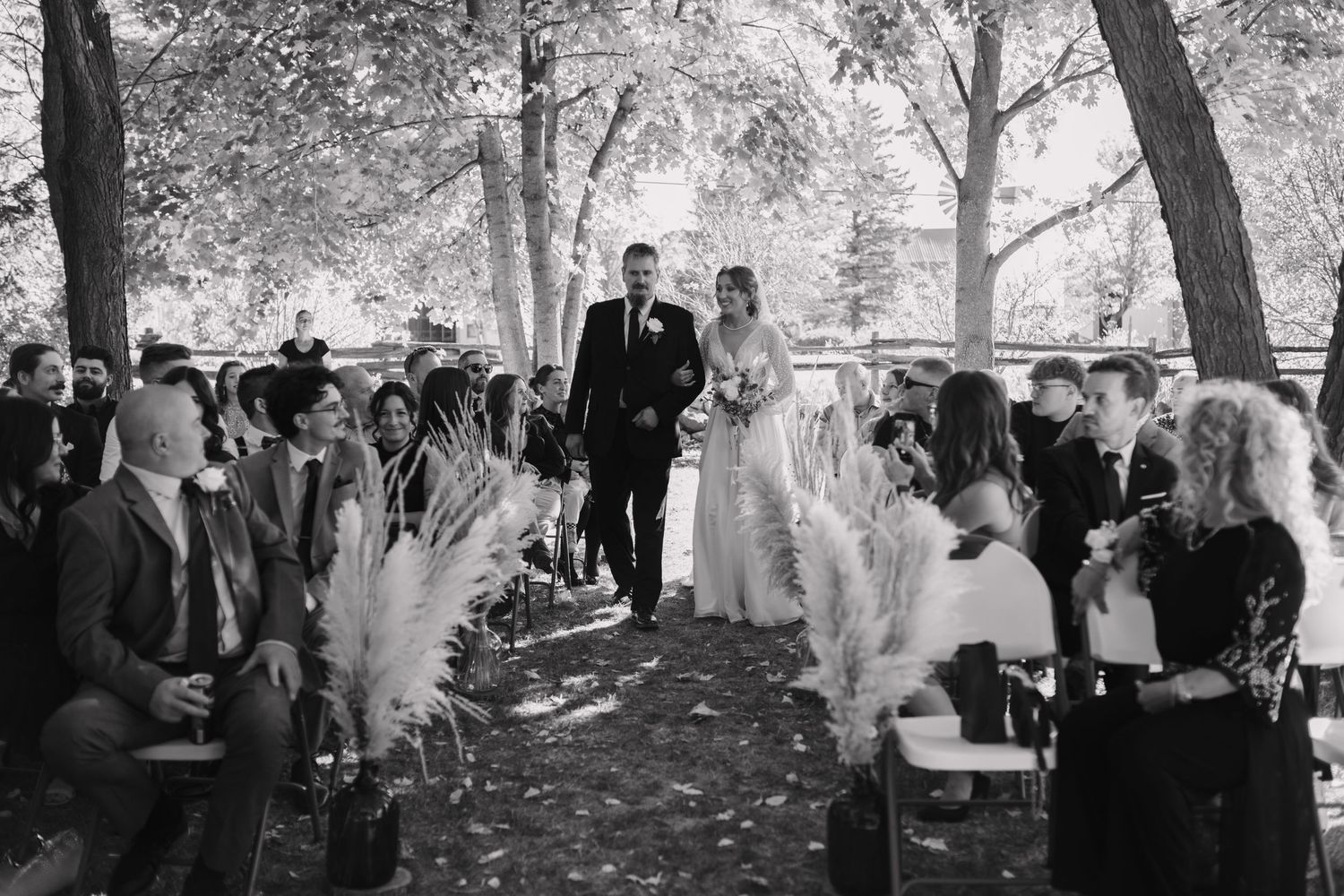 Bride and groom walk down the aisle at an outdoor wedding ceremony lined with pampas grass.