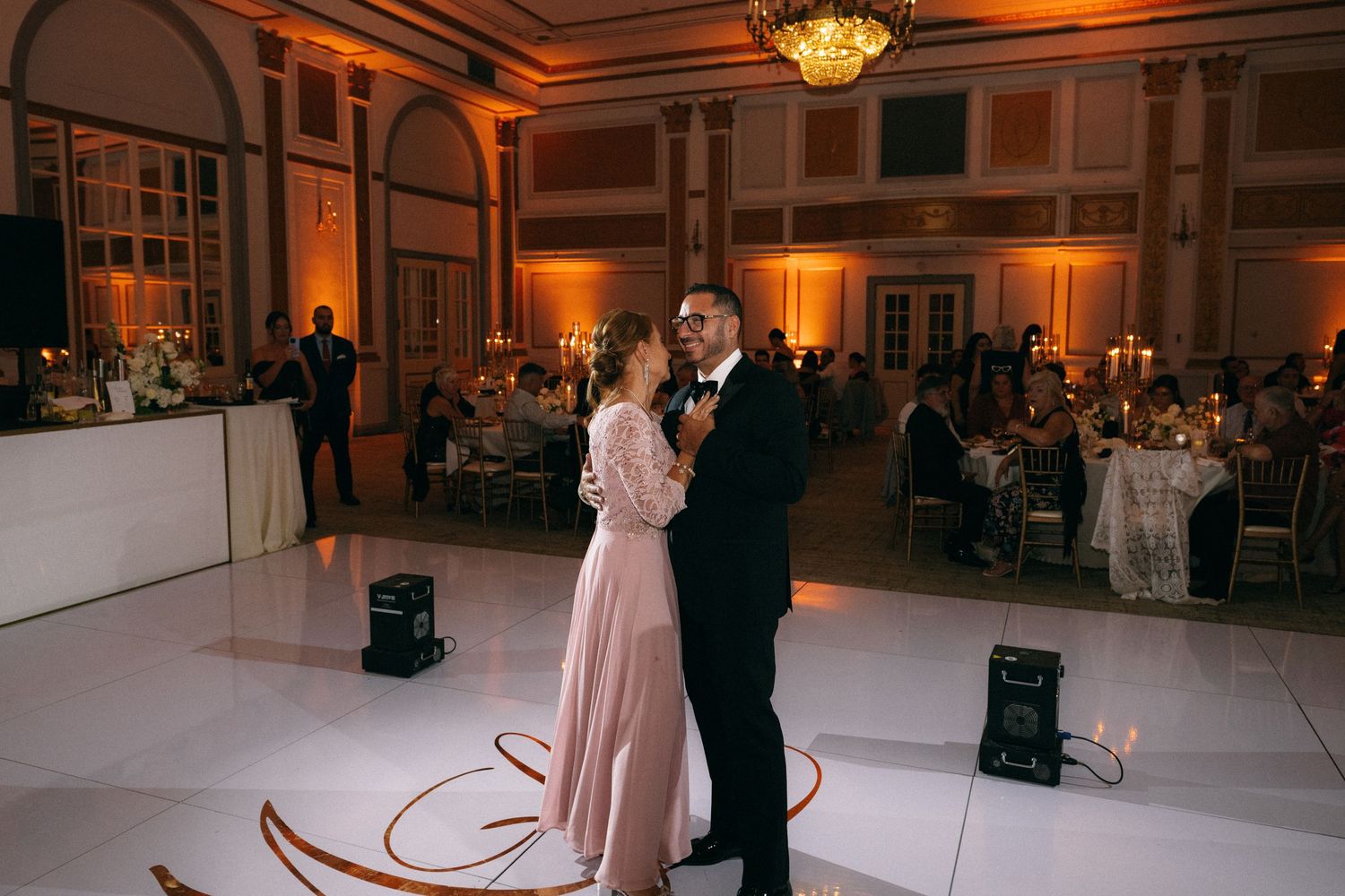 Couple shares first dance in elegant ballroom with warm golden lighting at wedding reception.