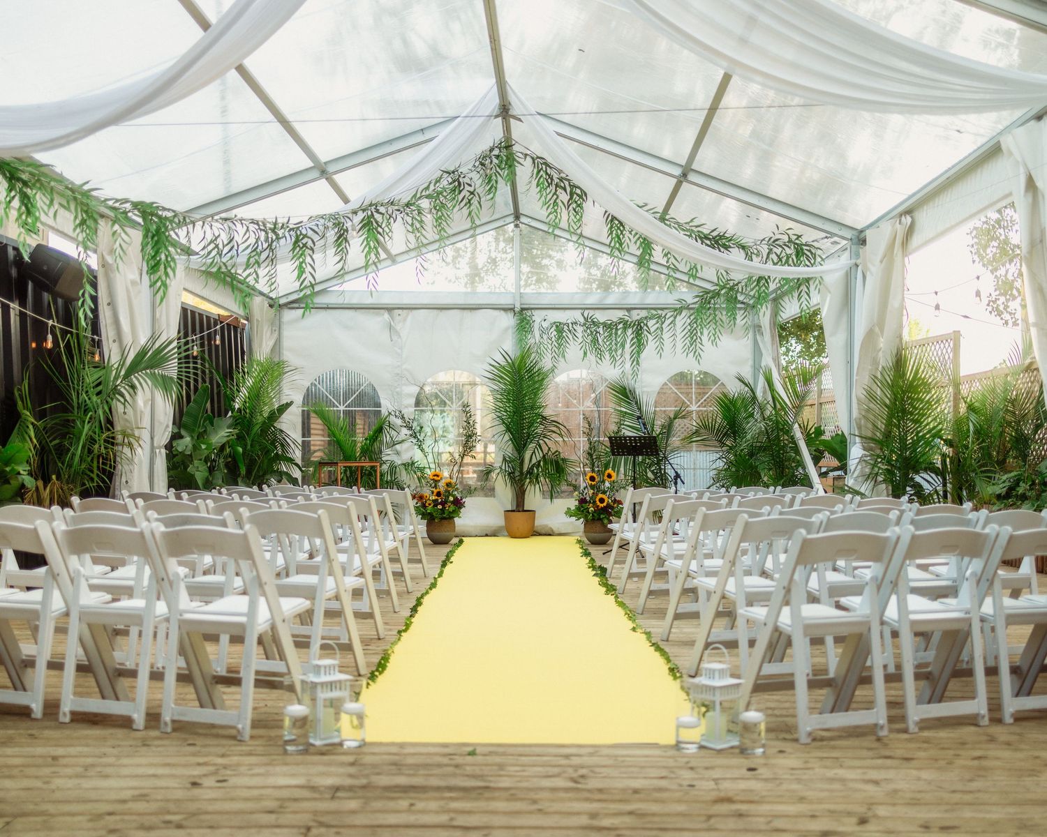 Elegant wedding ceremony venue under a clear tent with white chairs and a yellow aisle runner.