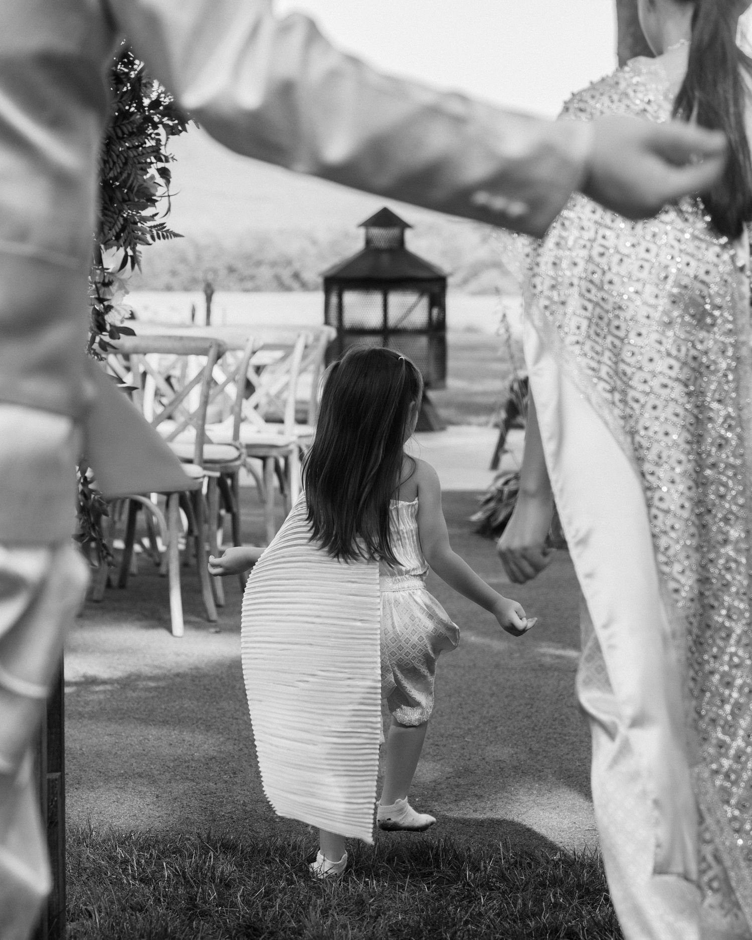 Black and white photo of a young girl in a striped dress at an outdoor wedding ceremony.