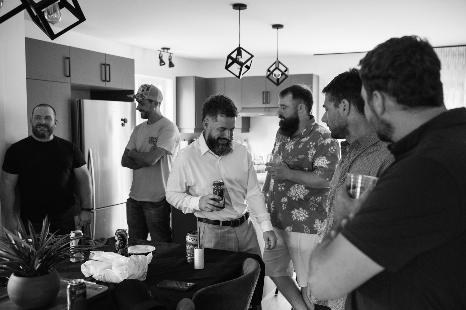 Black and white photo of a group of bearded men socializing in a modern kitchen during a casual gathering.