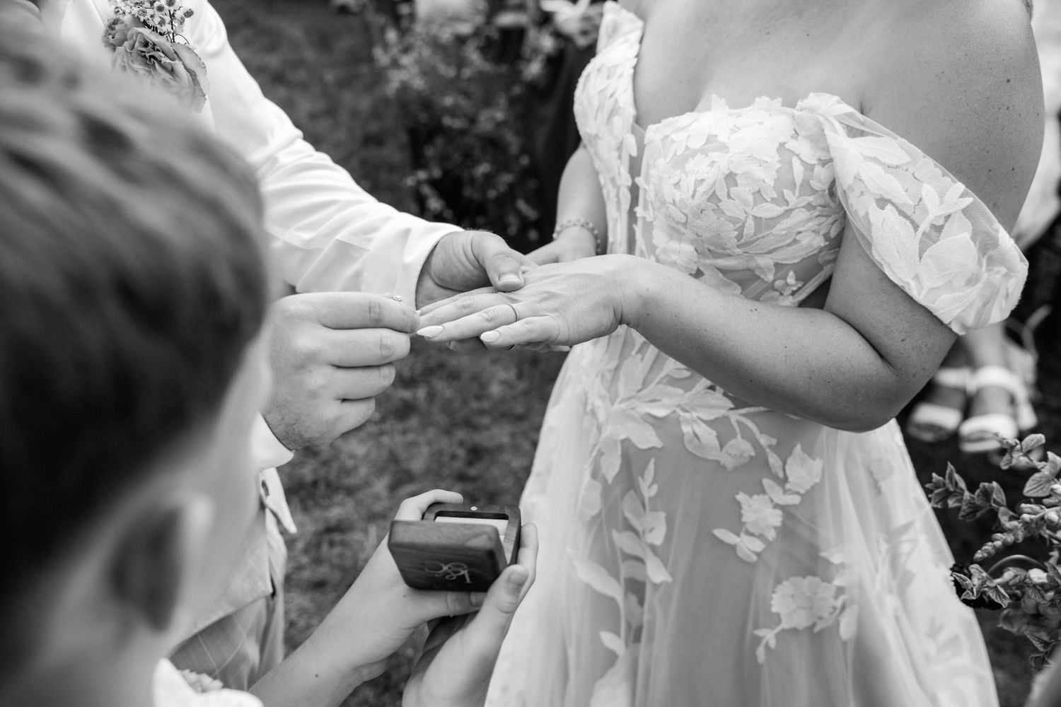 Black and white photo of wedding ring exchange ceremony outdoors.