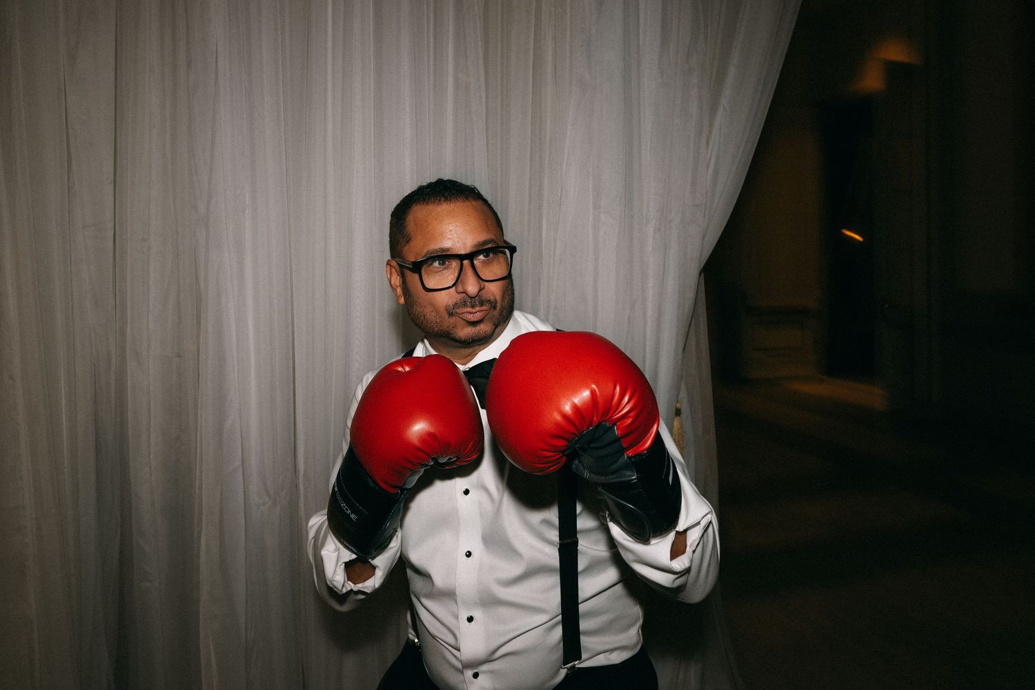 Wedding guest poses playfully wearing red boxing gloves in a tuxedo shirt at the reception.