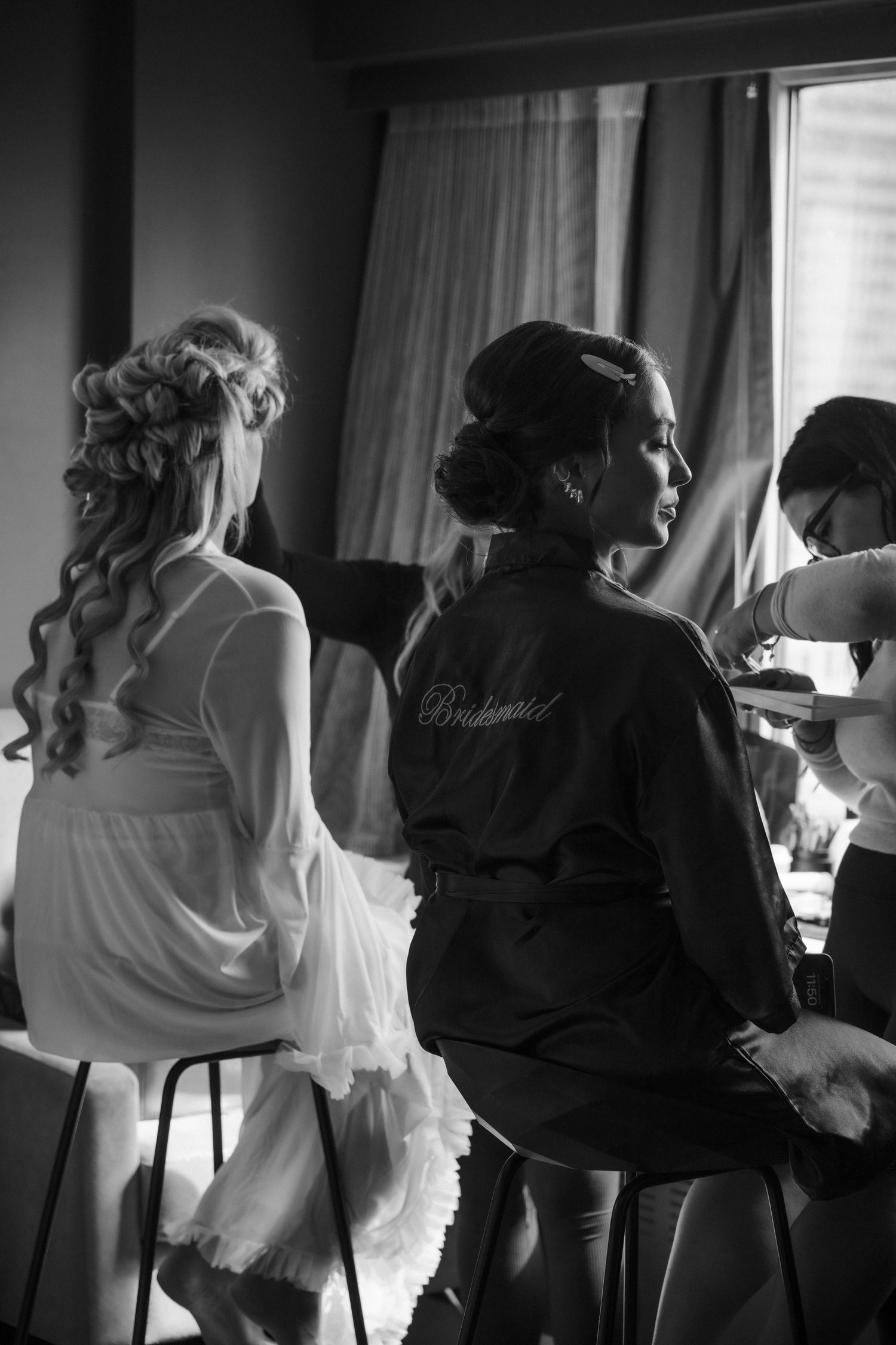 Bride and bridesmaid in robes getting ready together in a hotel room on wedding day.
