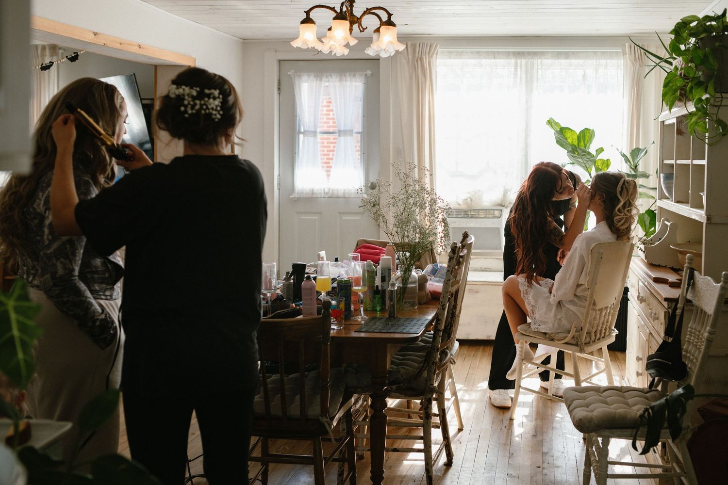 Bridesmaids help bride get ready in a warmly lit dining room before the wedding ceremony.