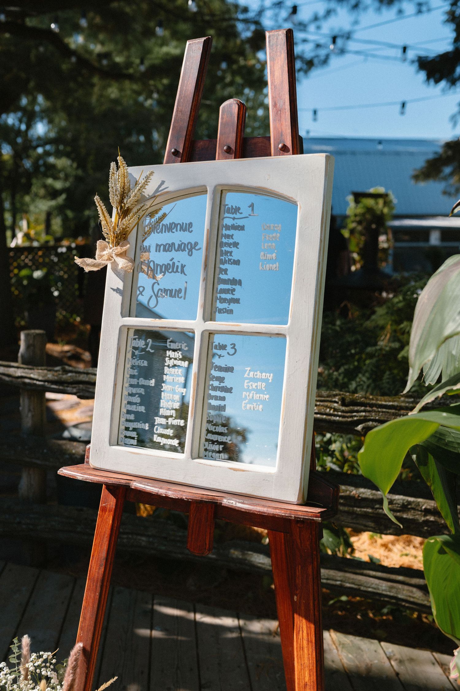 Rustic wedding seating chart displayed on a vintage window frame on a wooden easel outdoors.