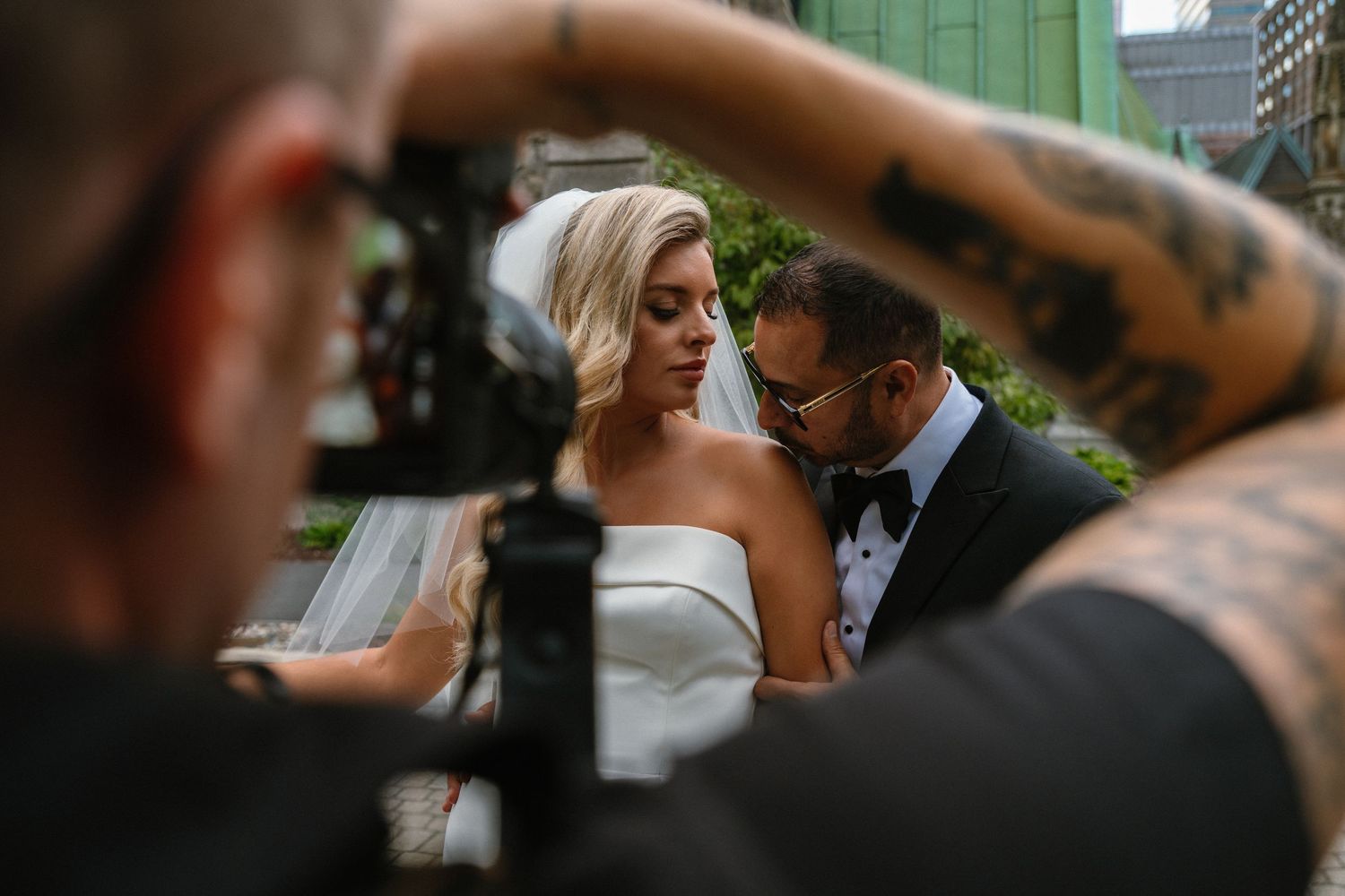 Tattooed photographer captures intimate moment between bride in strapless gown and groom in black suit at wedding.