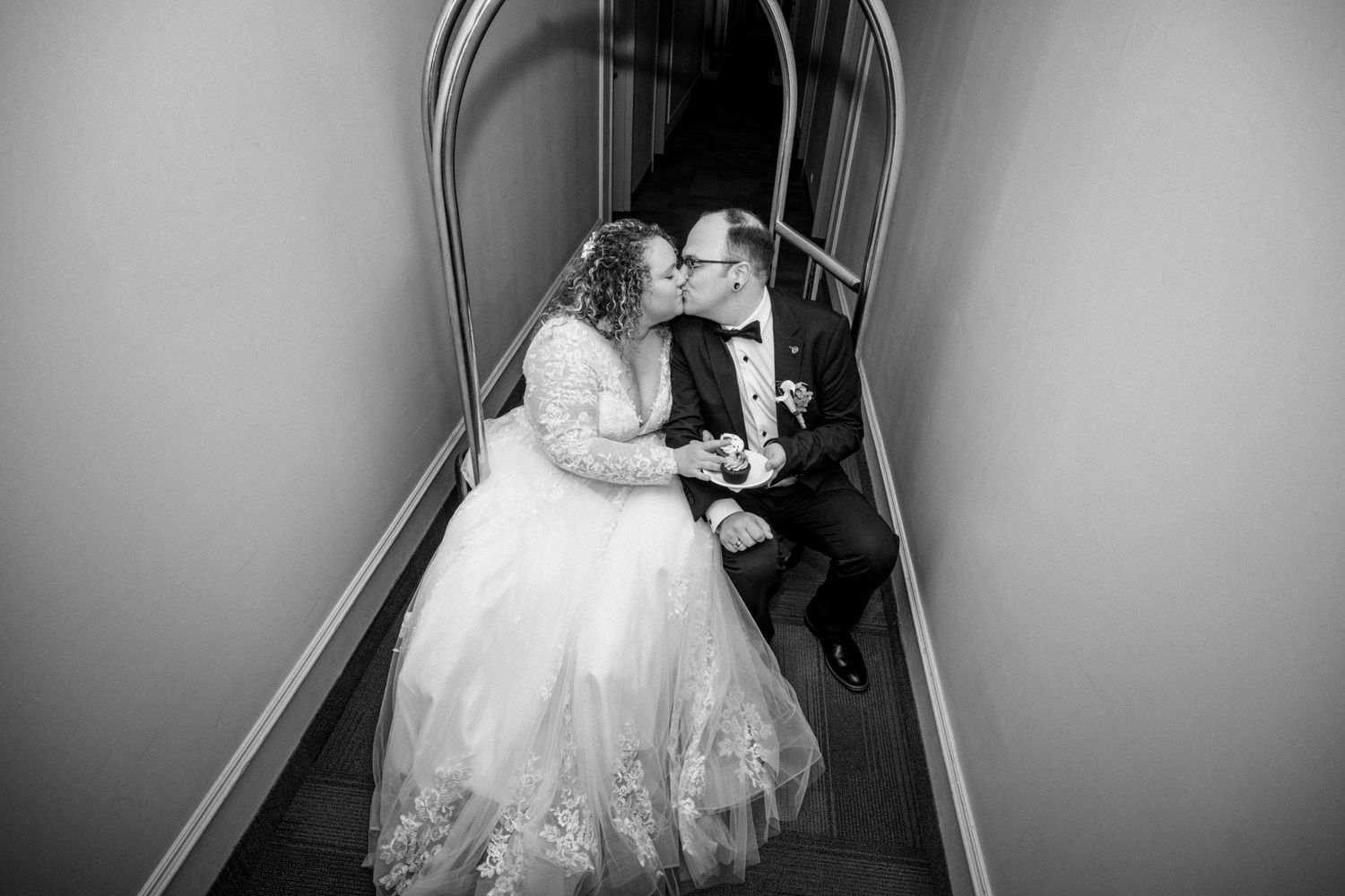 Black and white photo of bride and groom sharing a kiss on a staircase in wedding attire.