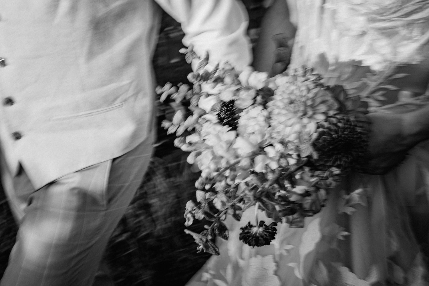 Black and white artistic shot of bride and groom holding lush wedding bouquet of wildflowers.
