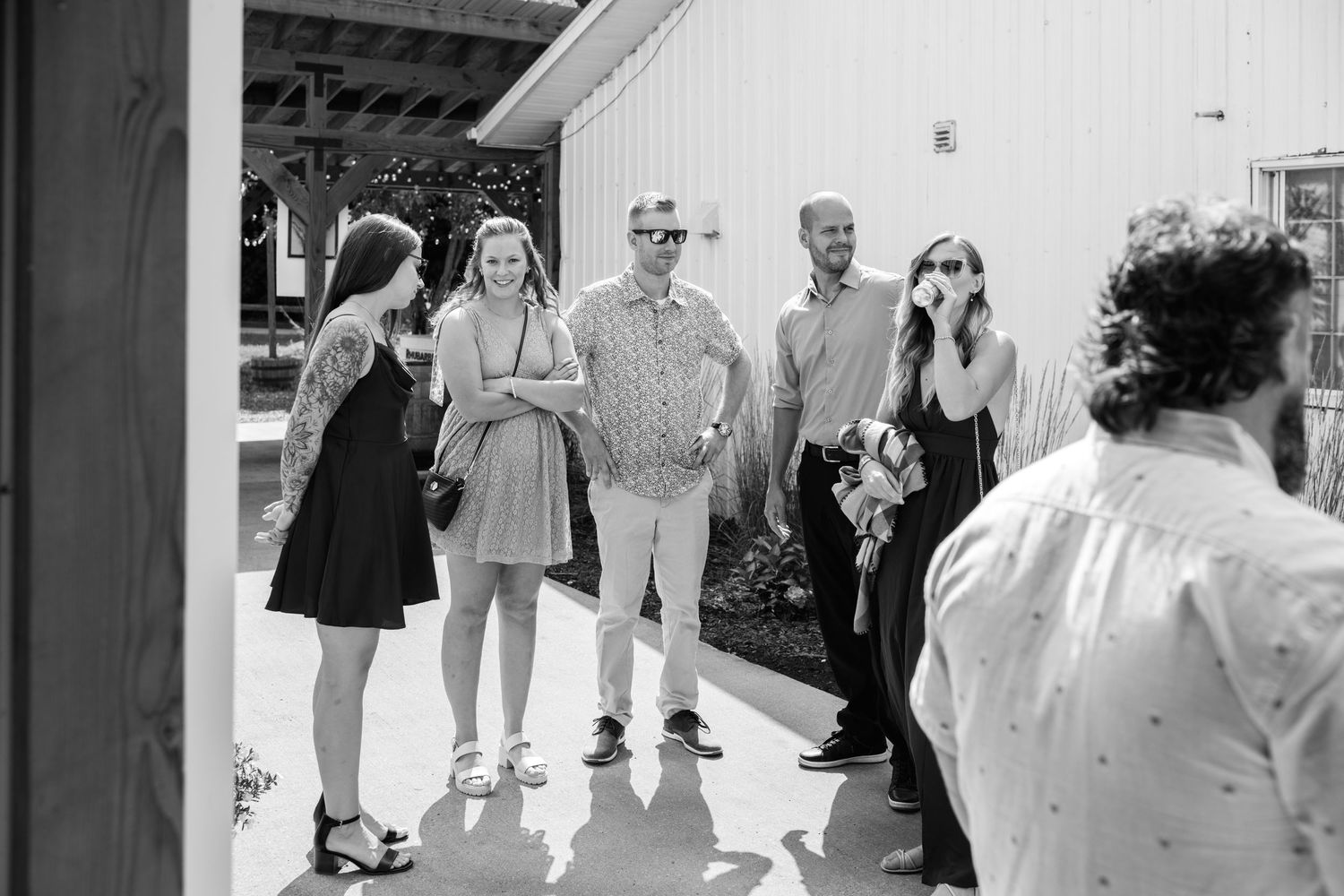 Black and white photo of a group of people socializing outdoors near a white barn building.