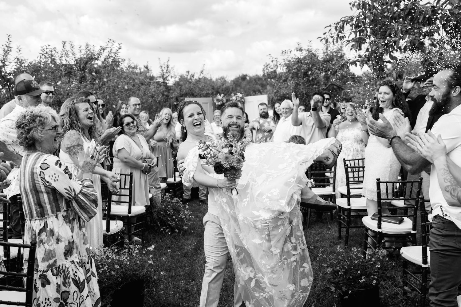 Joyful newlyweds walk back down the aisle as guests celebrate at an outdoor wedding ceremony.