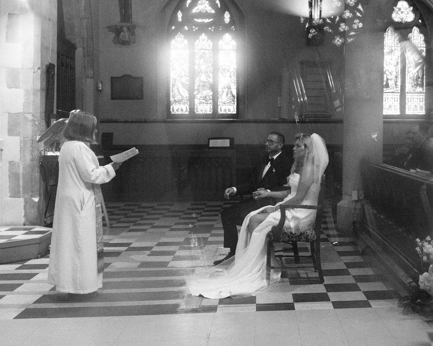 Black and white photo of bride and groom seated during church wedding ceremony.
