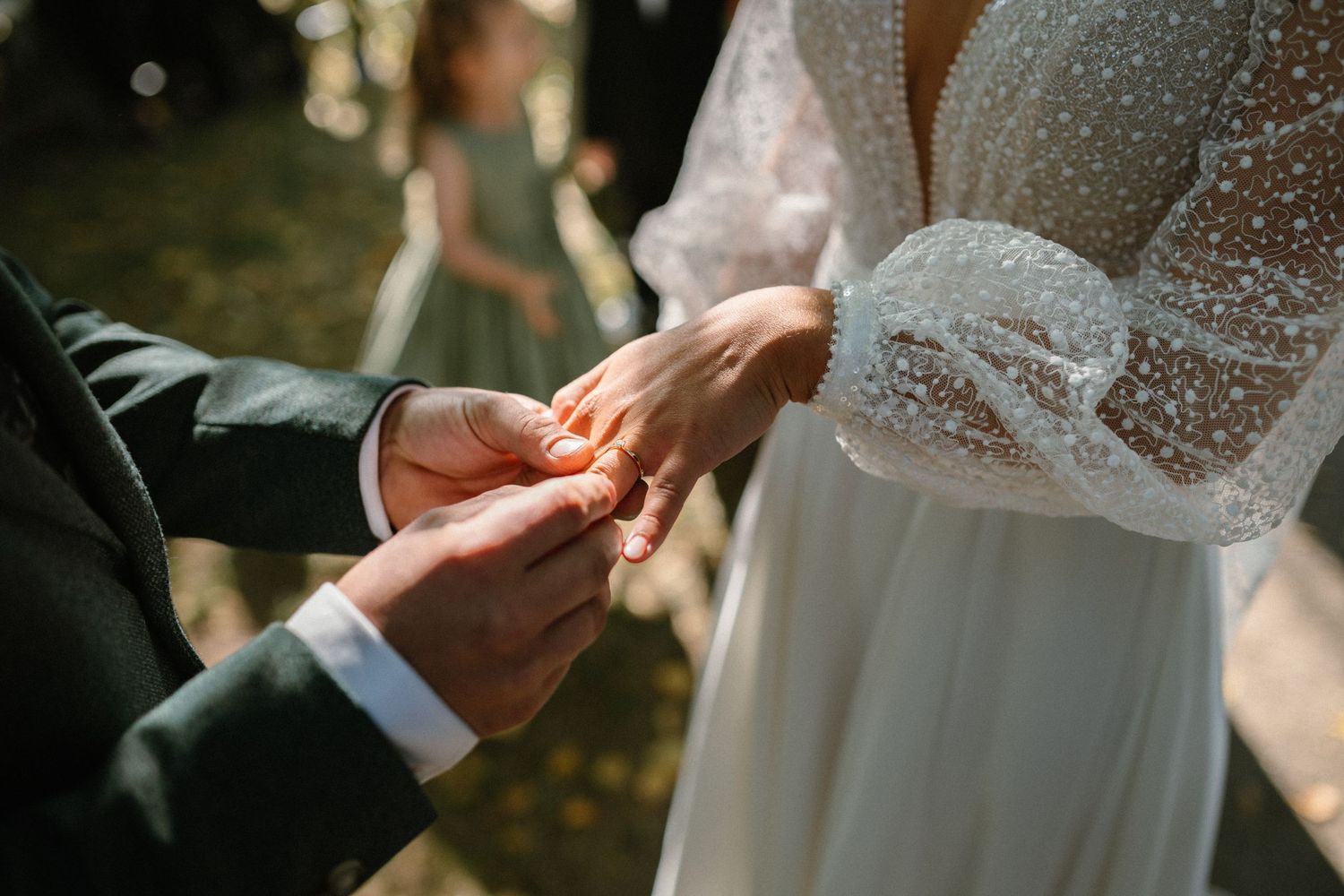 Groom placing a wedding ring on bride's finger during an outdoor wedding ceremony.