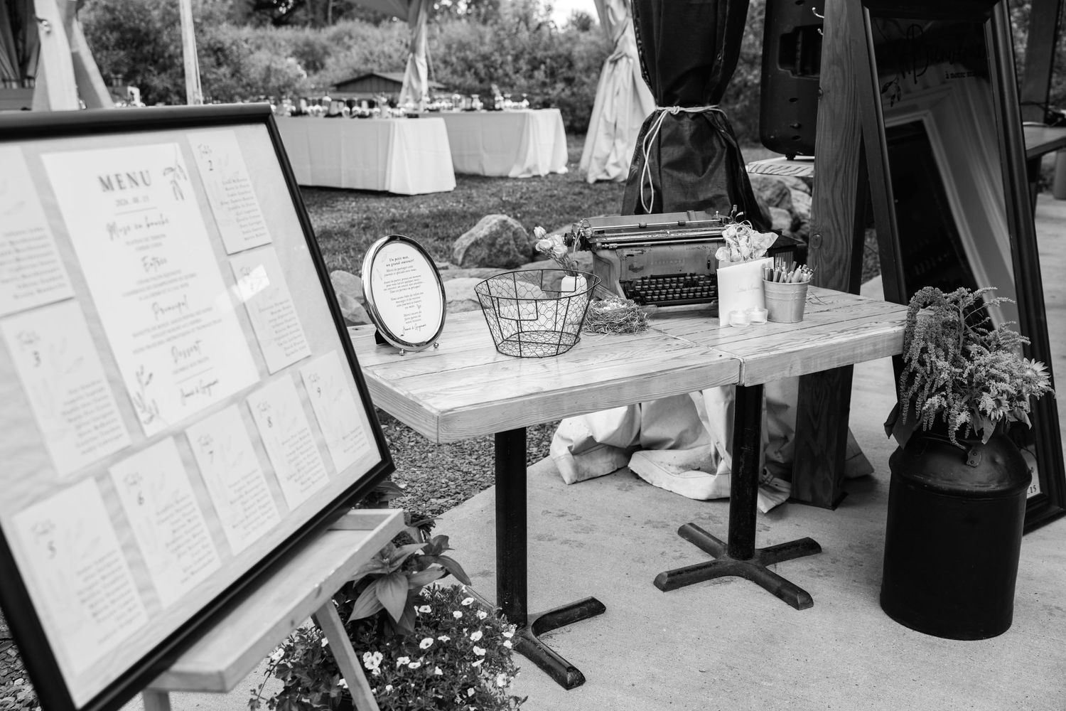 Black and white photo of an outdoor wedding reception table display with menu boards and decorative items.