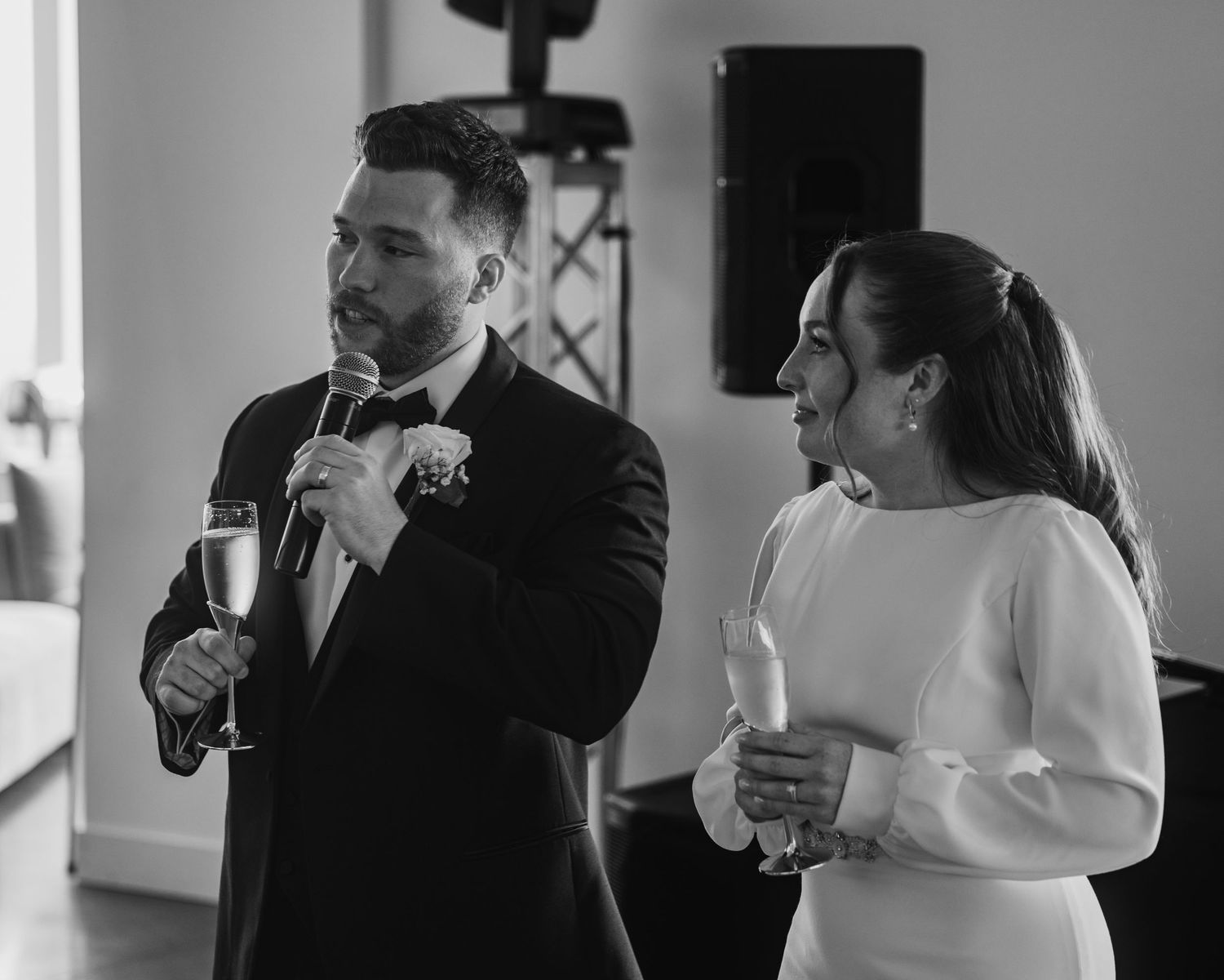 Black and white photo of a bride and groom holding champagne glasses during their wedding reception toast.