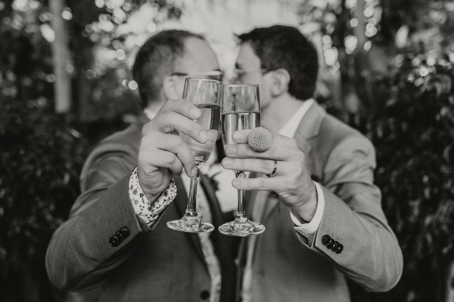 Two grooms in suits toasting with champagne glasses at their wedding celebration in black and white.