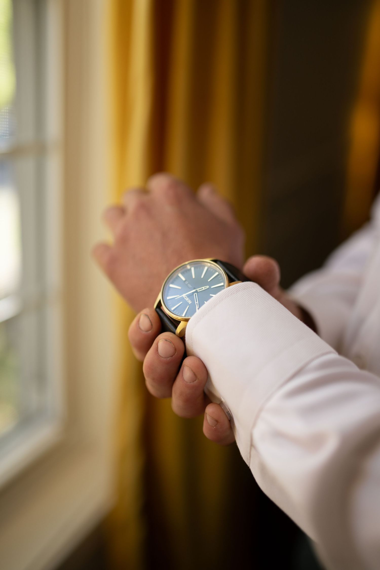 Groom adjusting his gold watch with blue face on his wrist before wedding ceremony.