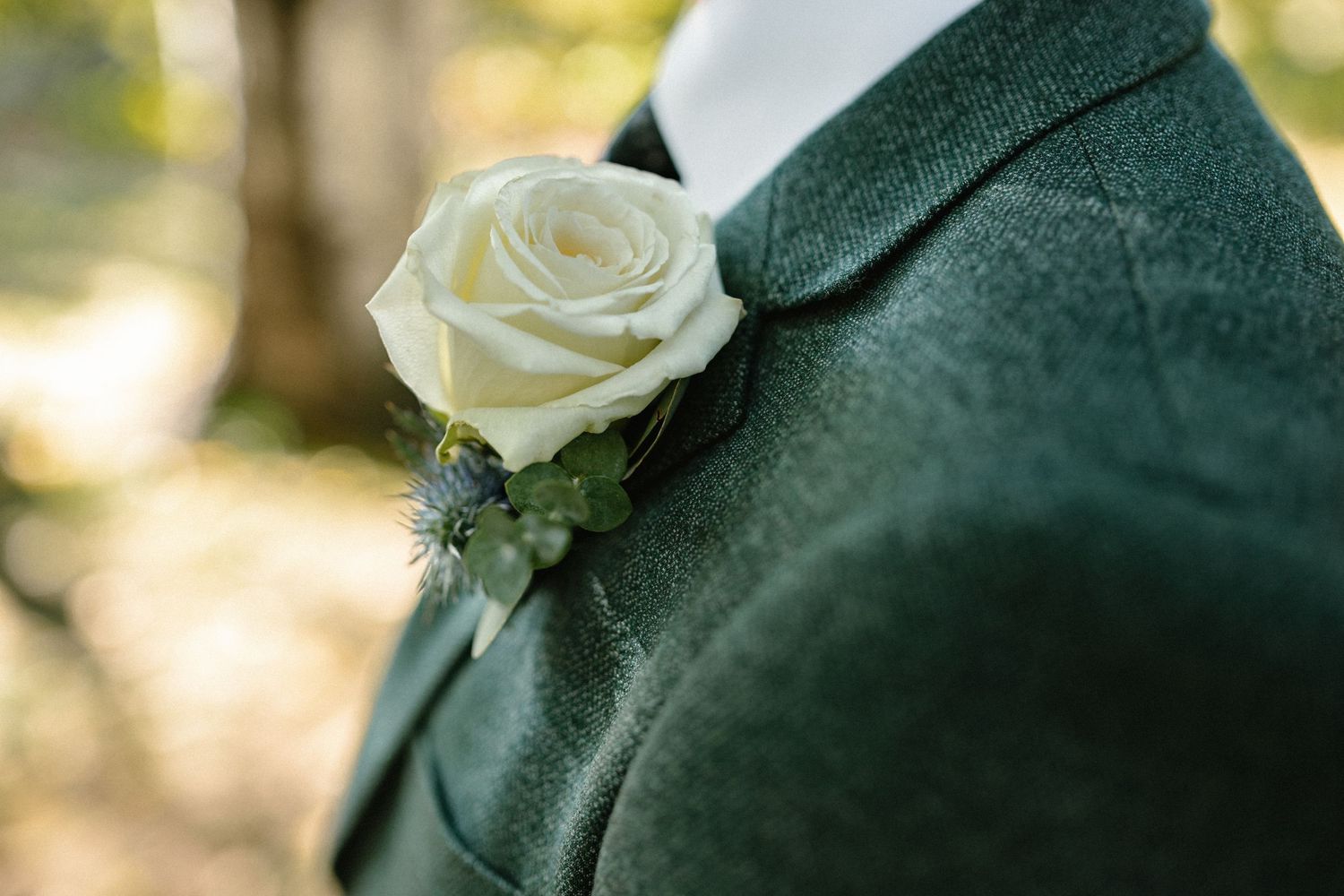 Close-up of a white rose boutonniere on a dark green wedding suit jacket.
