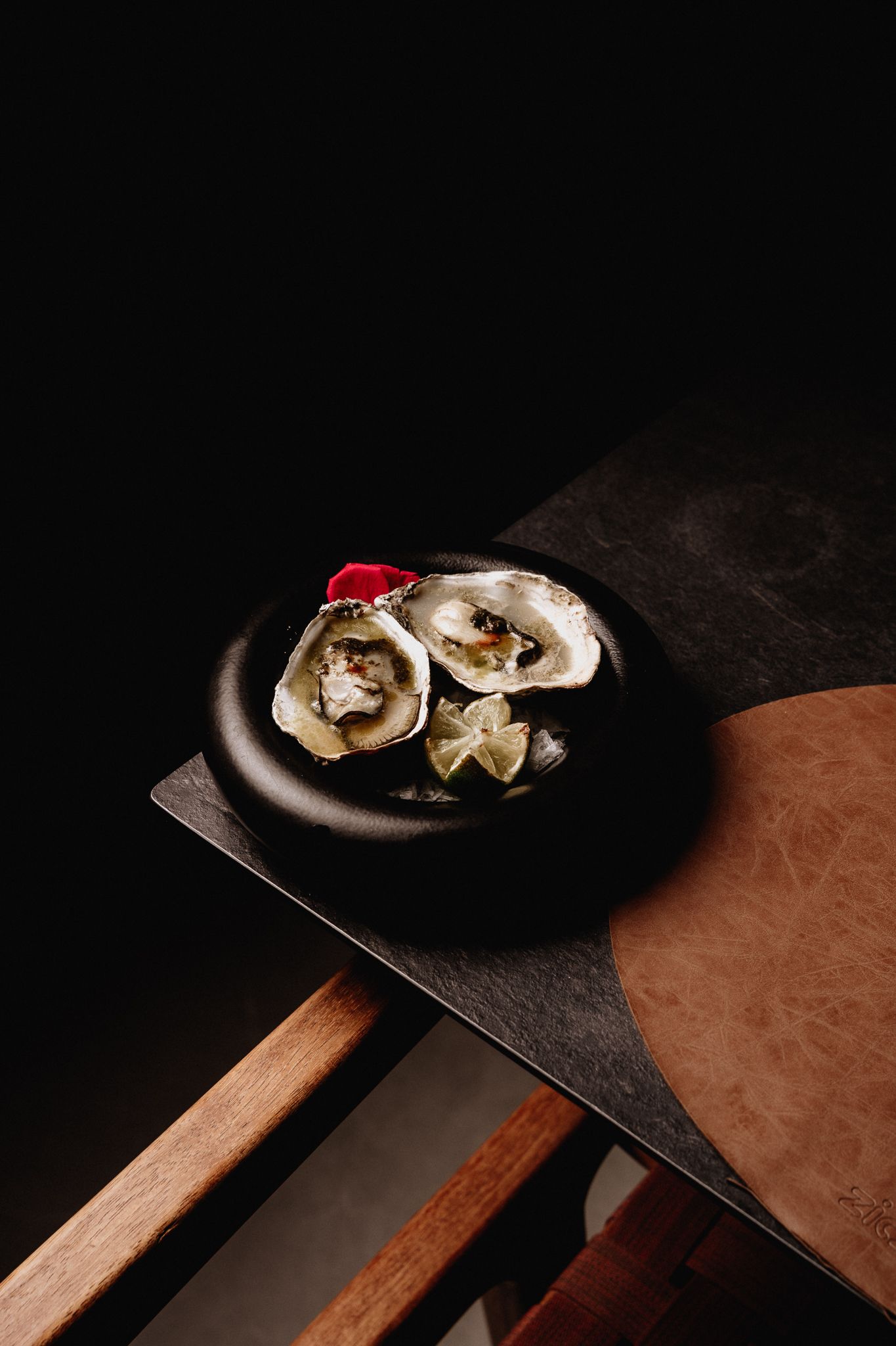 Two fresh oysters served on a dark ceramic plate with garnish on a slate board in dramatic lighting.