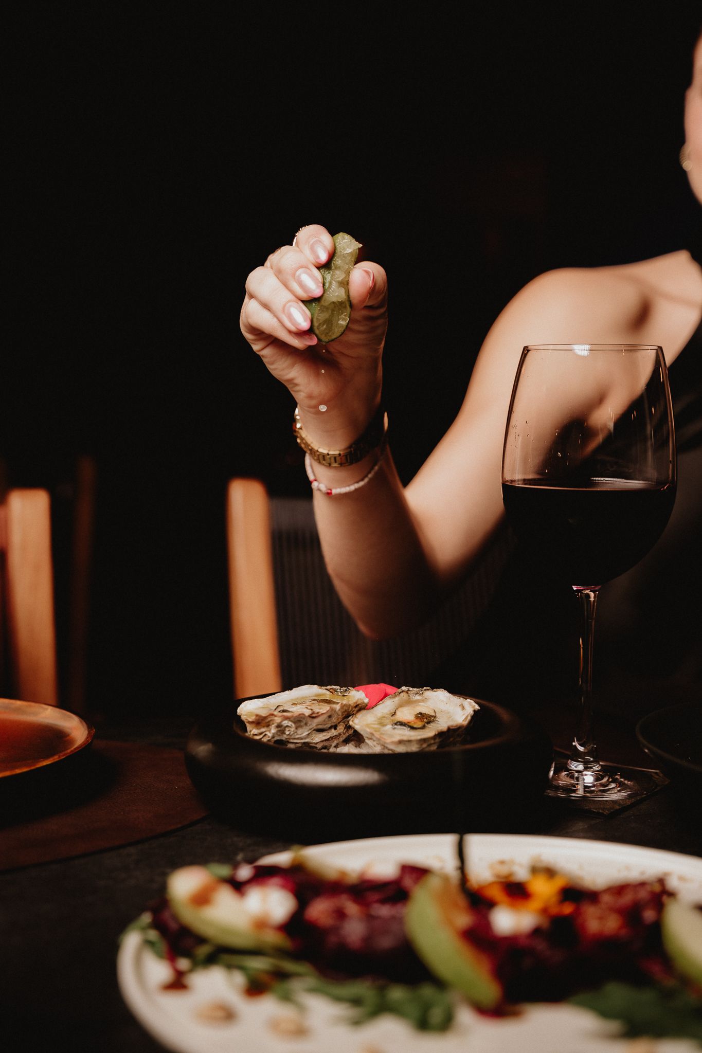 Woman squeezing lime over oysters with a glass of red wine at a fine dining restaurant.