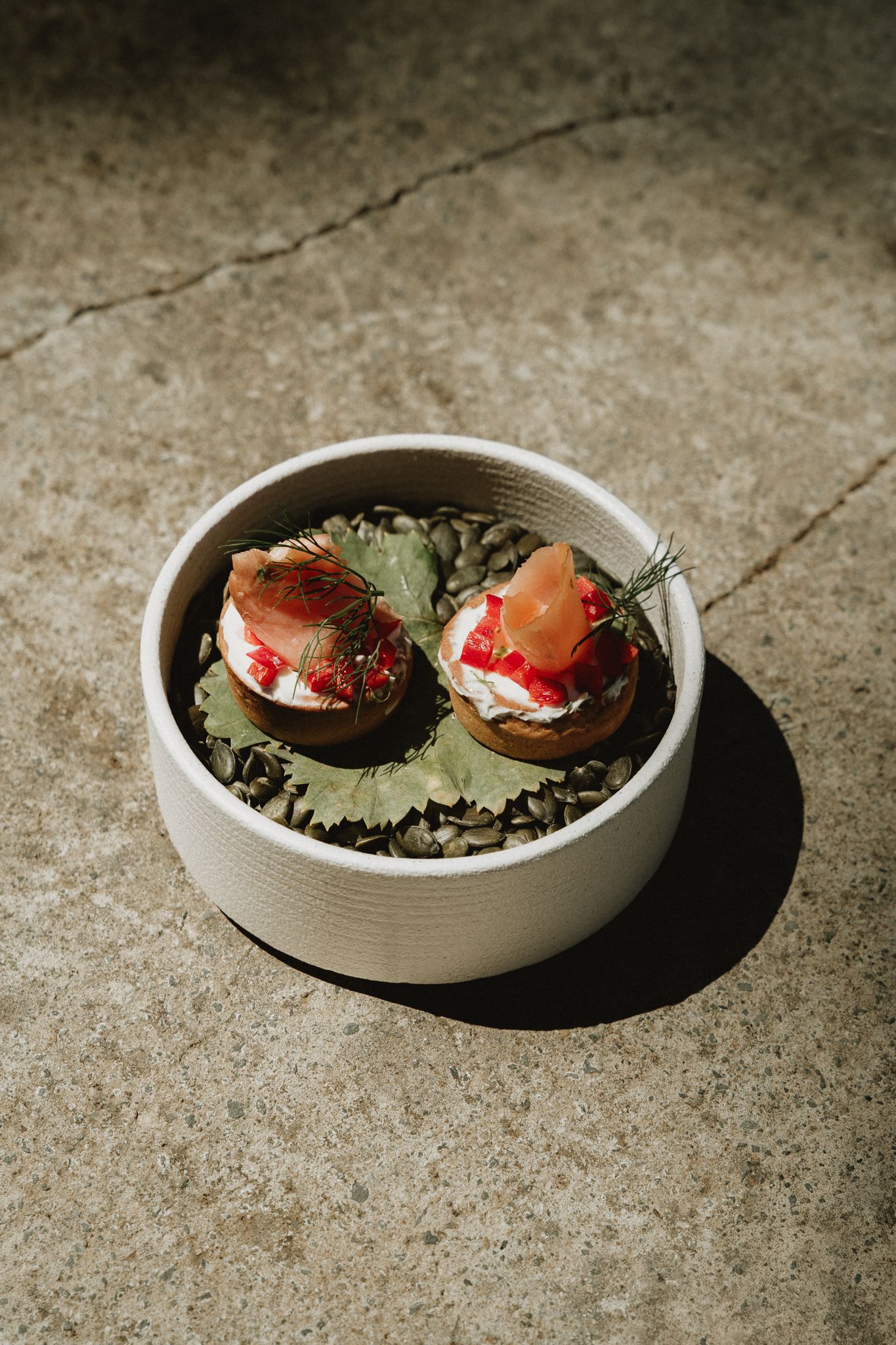 Two elegant smoked salmon canapes with cream cheese on a leaf bed in a white ceramic bowl, served outdoors.
