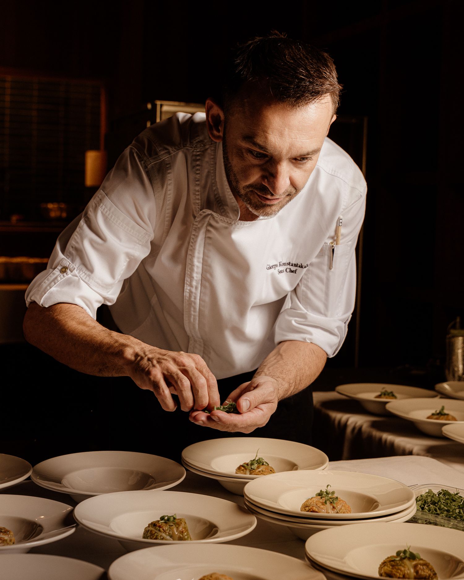 Chef carefully plates gourmet dishes in a professional kitchen wearing a white chef coat.