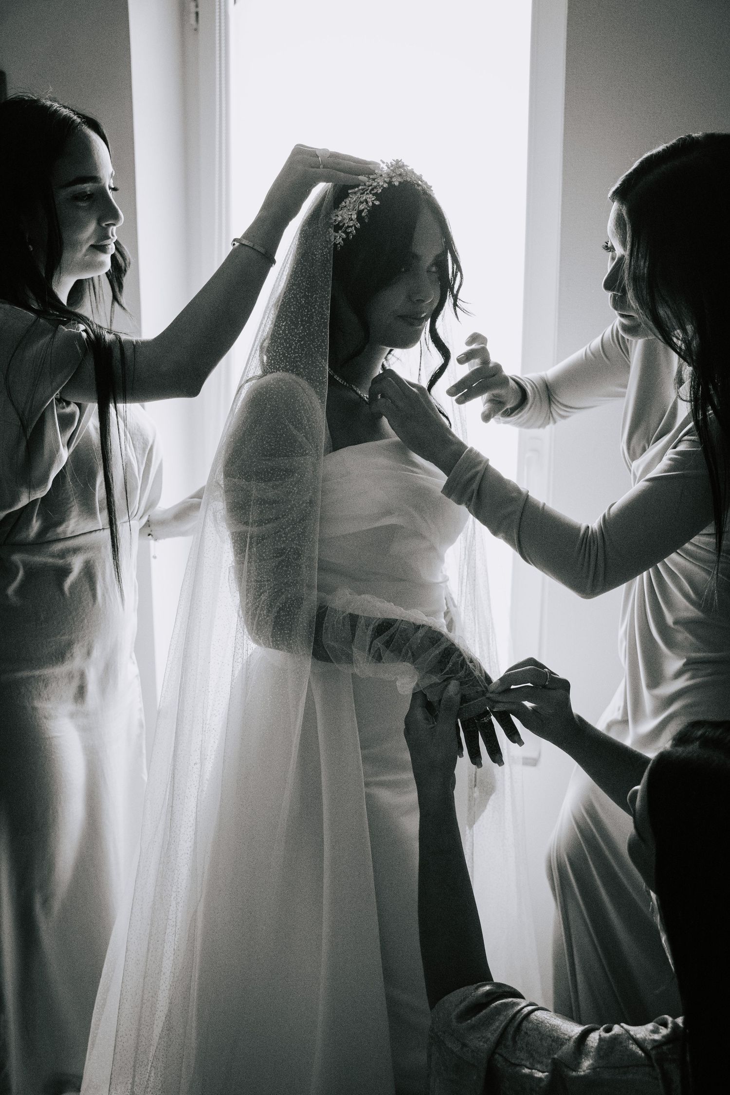 Black and white photo of bridesmaids helping bride with veil and tiara before the wedding.