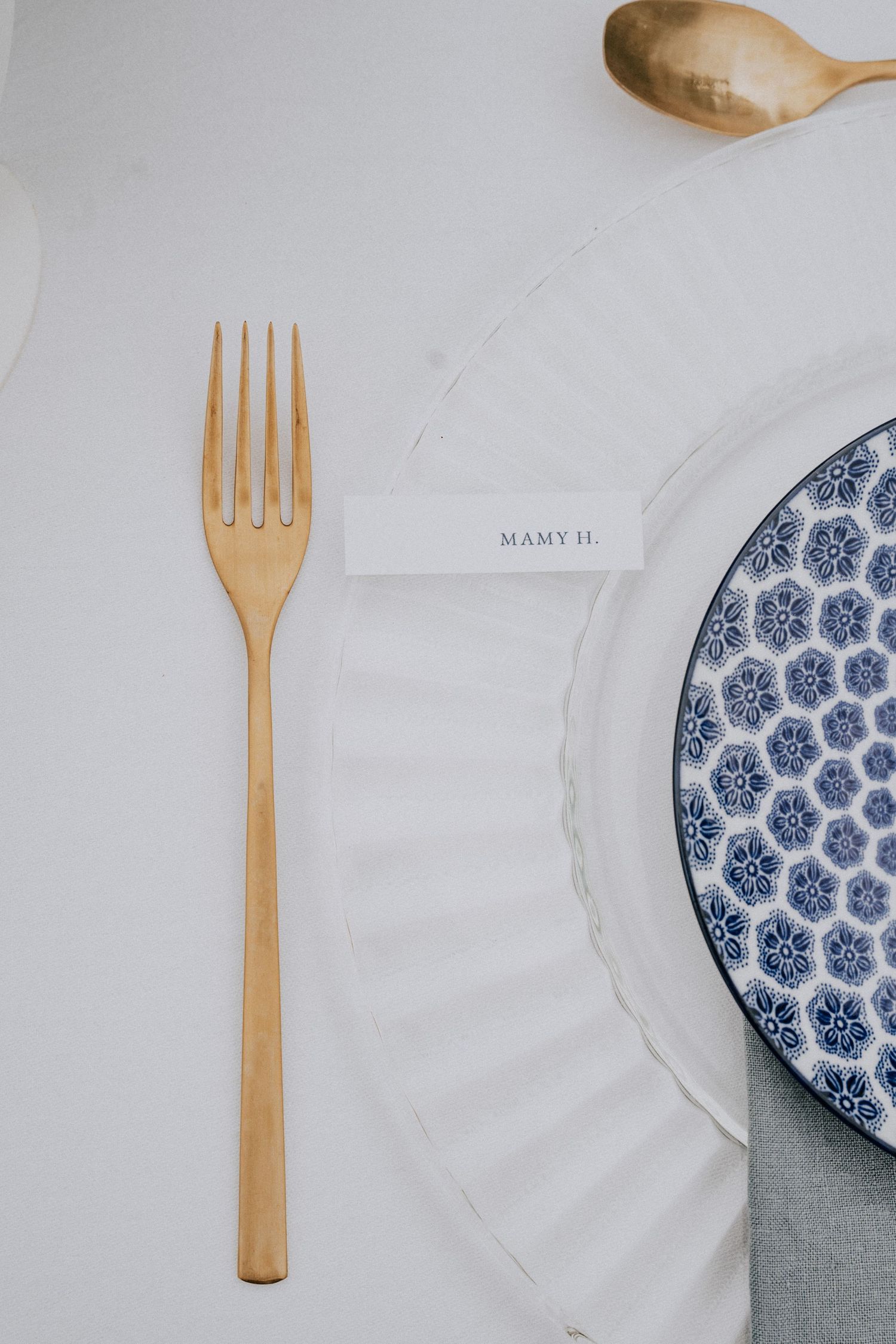 Gold fork and spoon beside blue patterned plate with place card reading MAMY H.