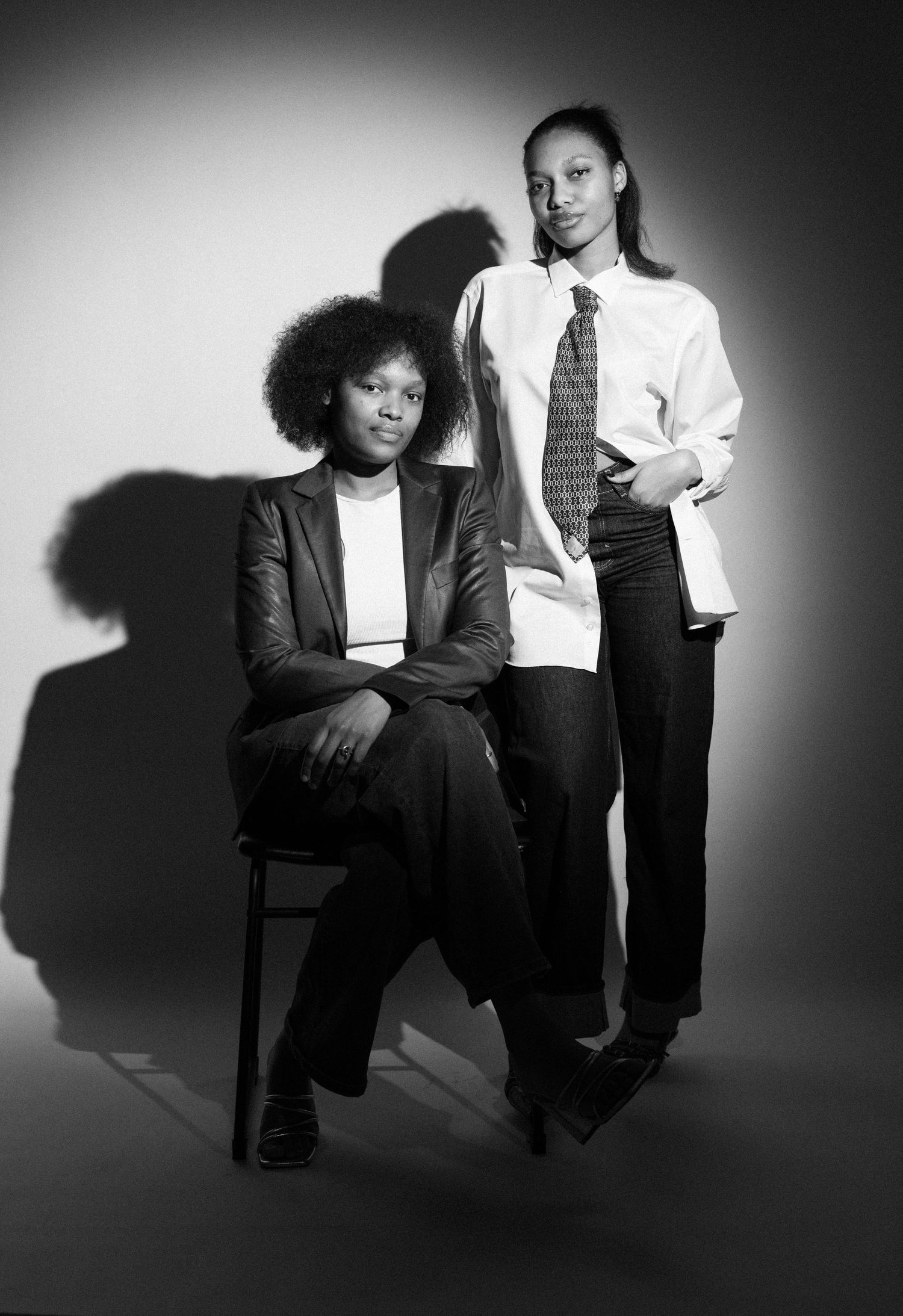 Black and white portrait of two young women posing confidently in blazer and white shirt with tie.