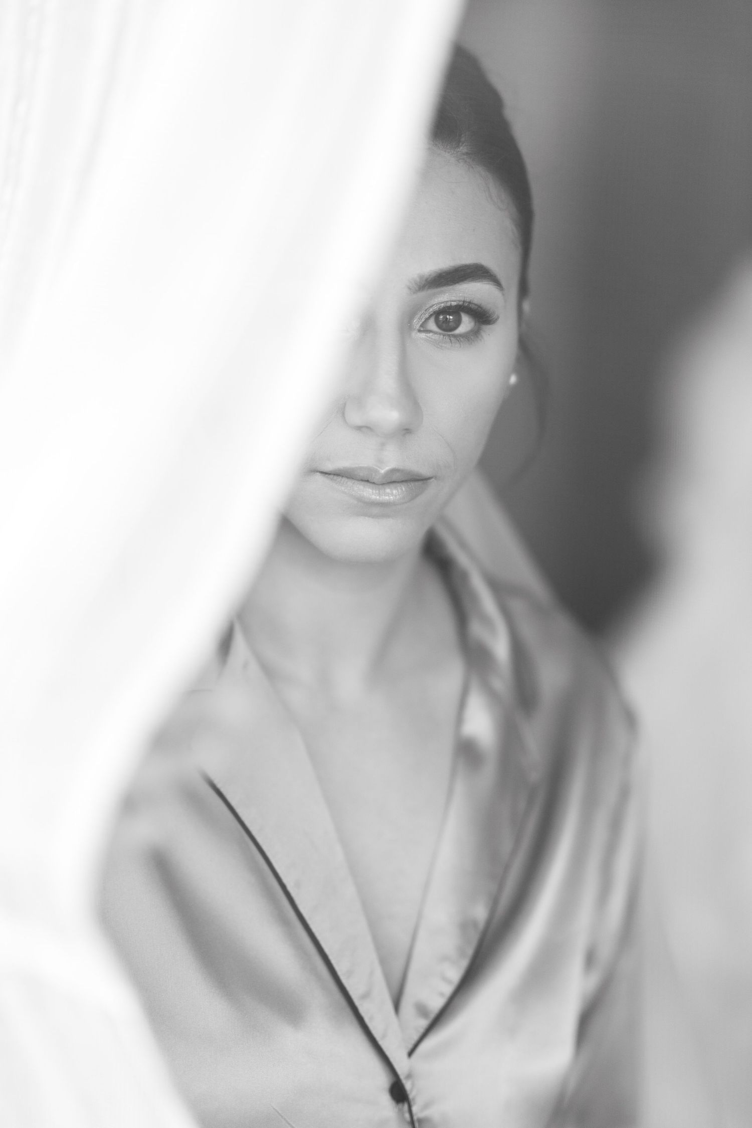 Stunning black and white close-up of bride in satin robe partially hidden by curtain.